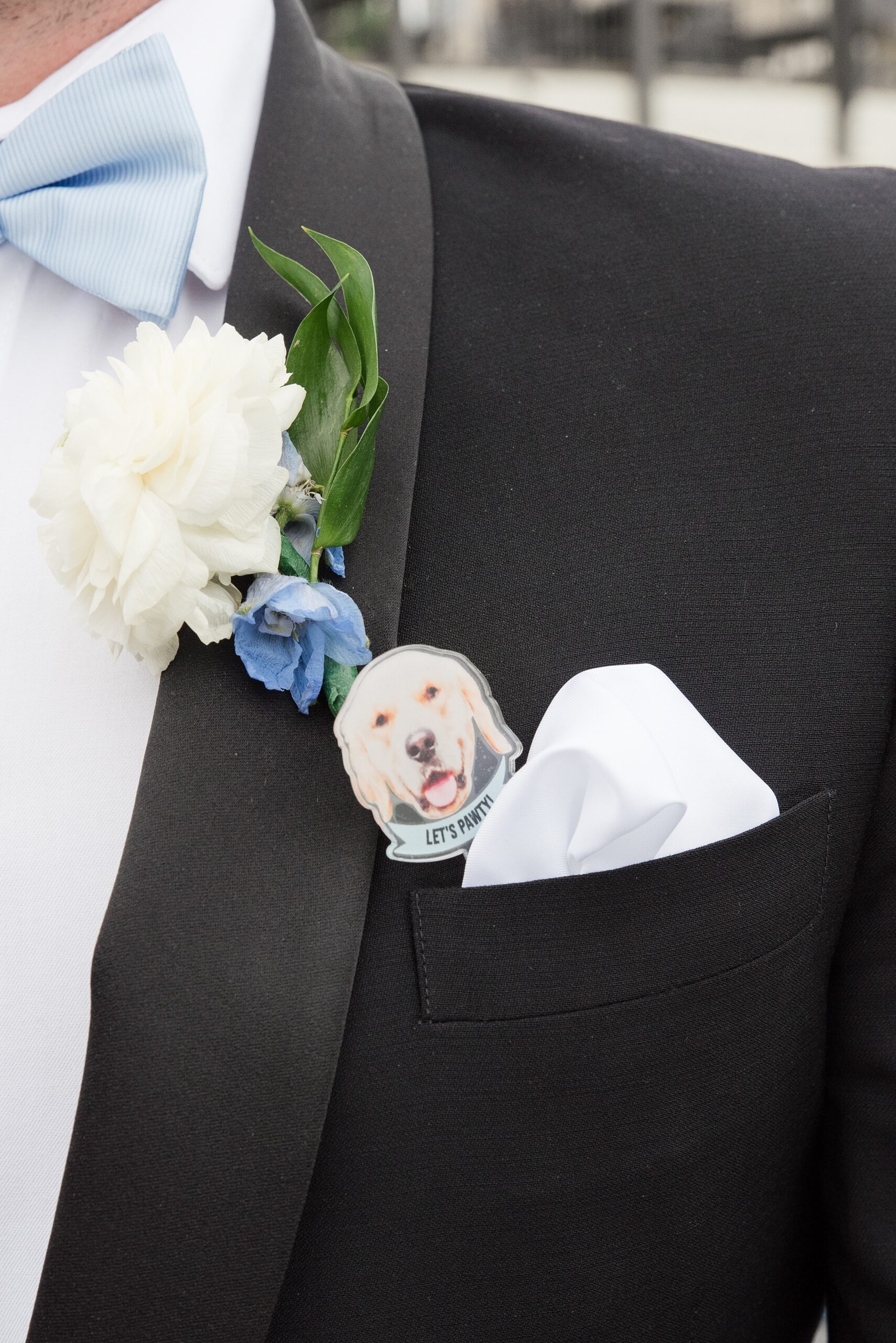 Details of a groom with a dog party favor in his pocket by a boutonniere