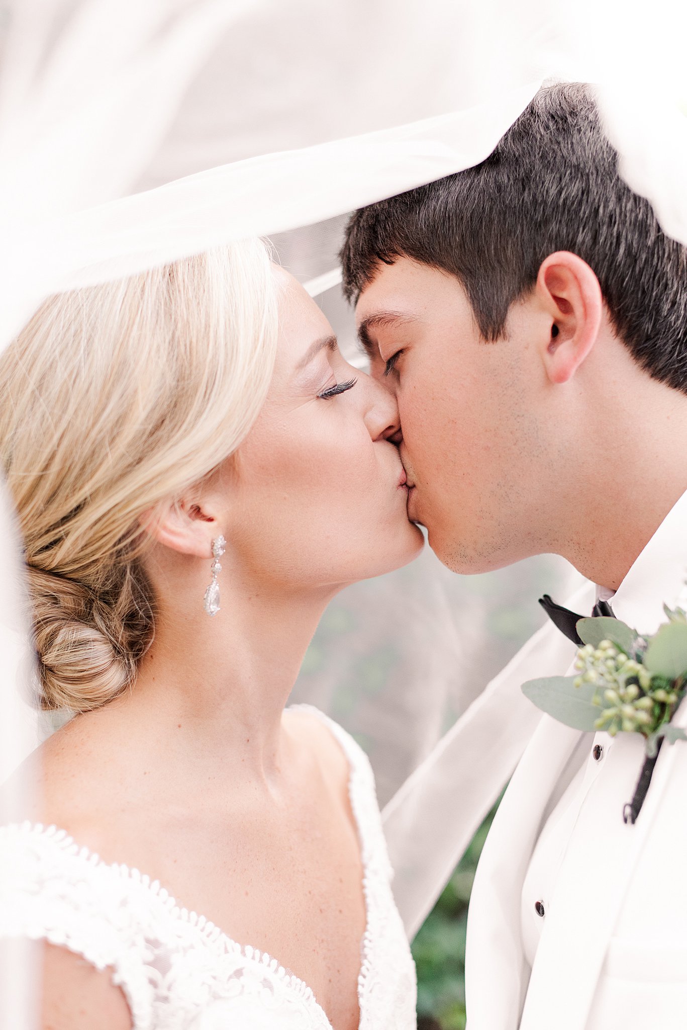 Newlyweds kiss while hiding under a veil in a white tuxedo and lace dress at their Belmont Manor Wedding