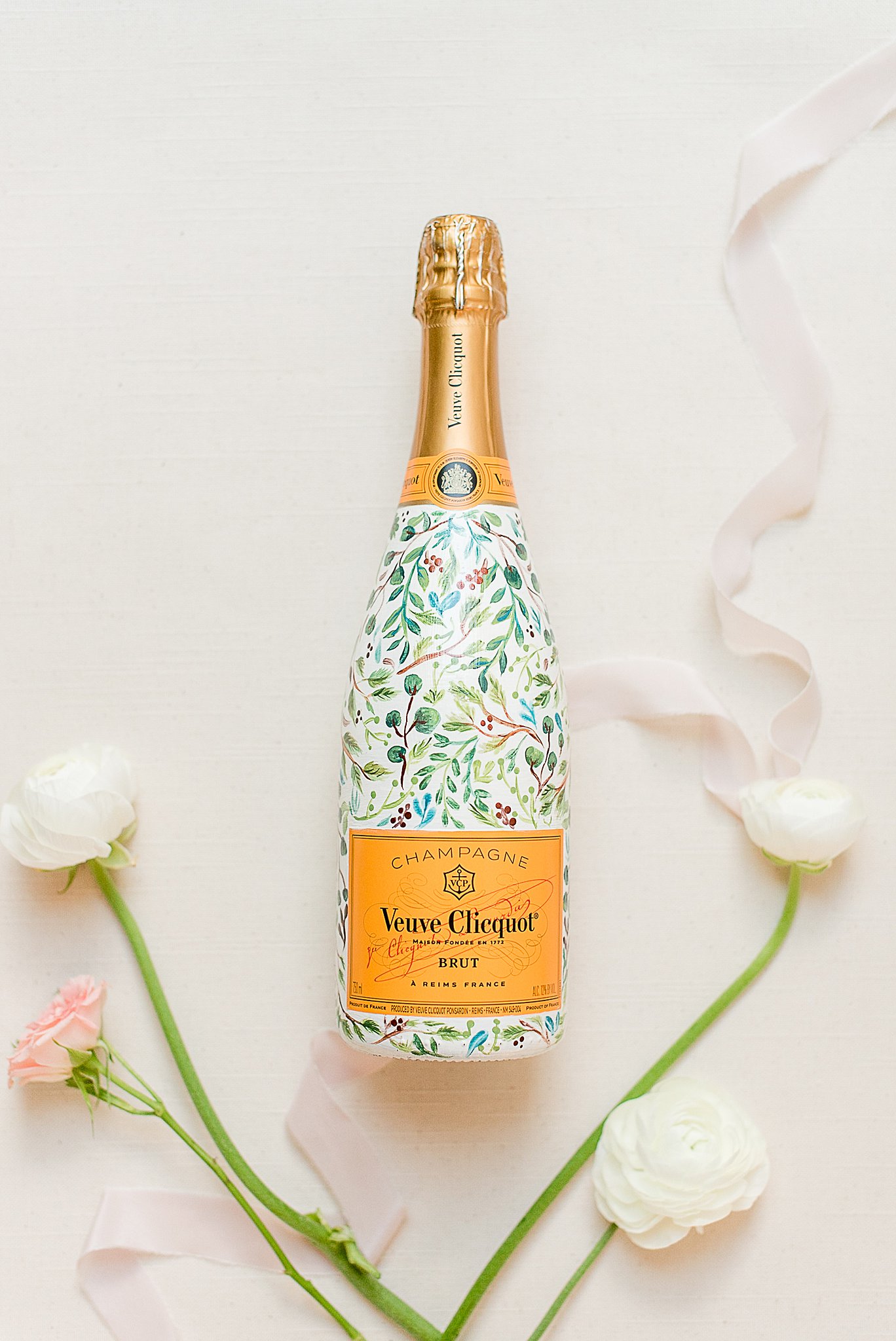 A bottle of colorful champagne lays on a table with white and pink flowers