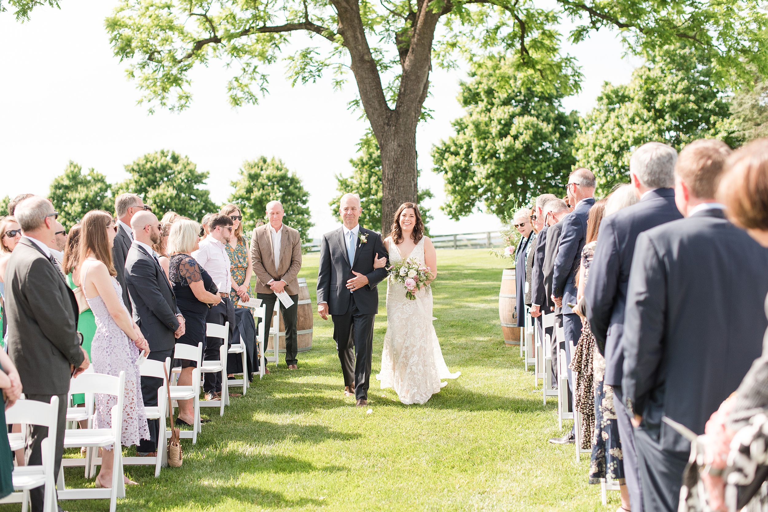 A father walks his daughter down the aisle at her outdoor Bluebird Manor wedding ceremony