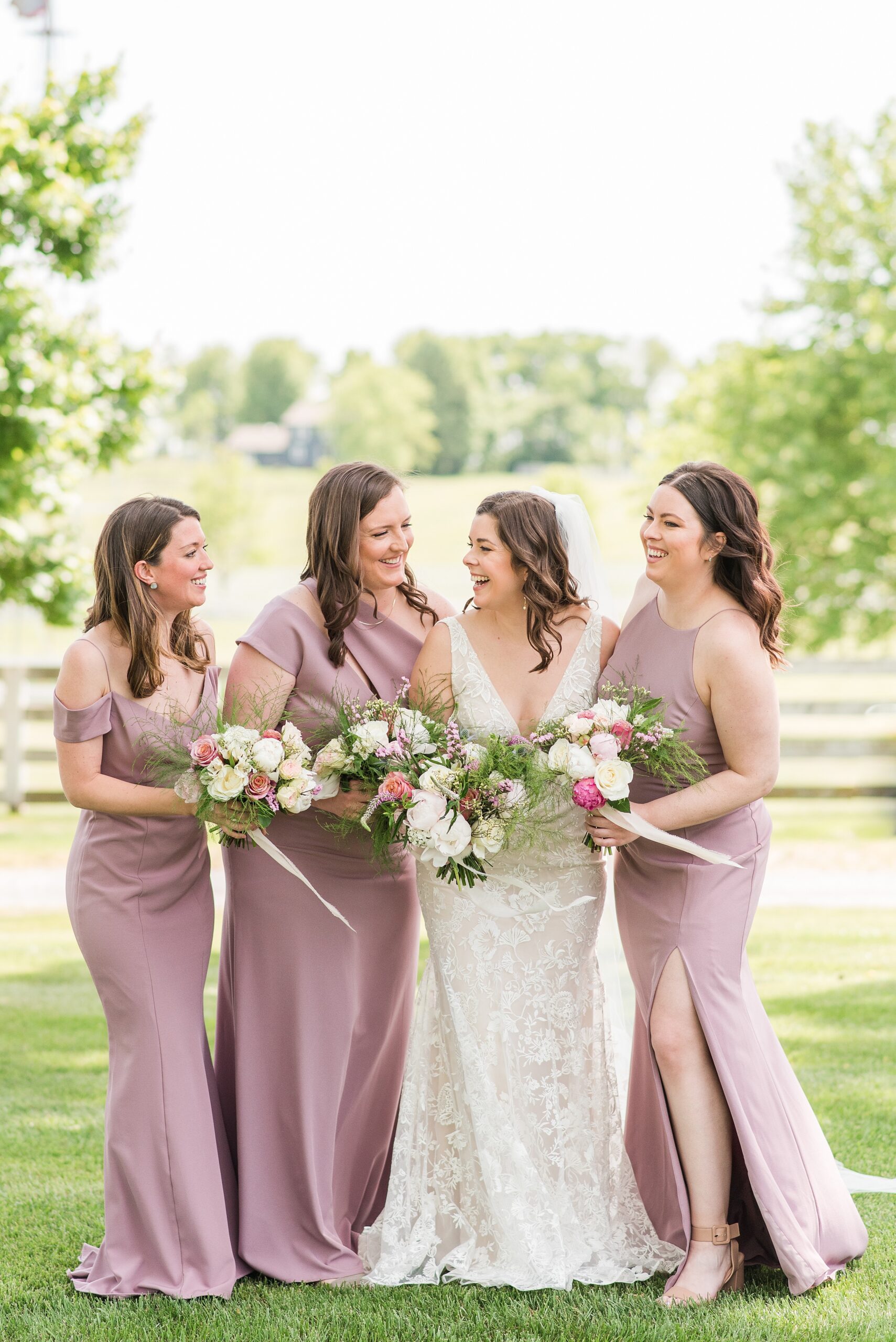 A bride laughs while standing in a lawn with her bridesmaids in pink dresses