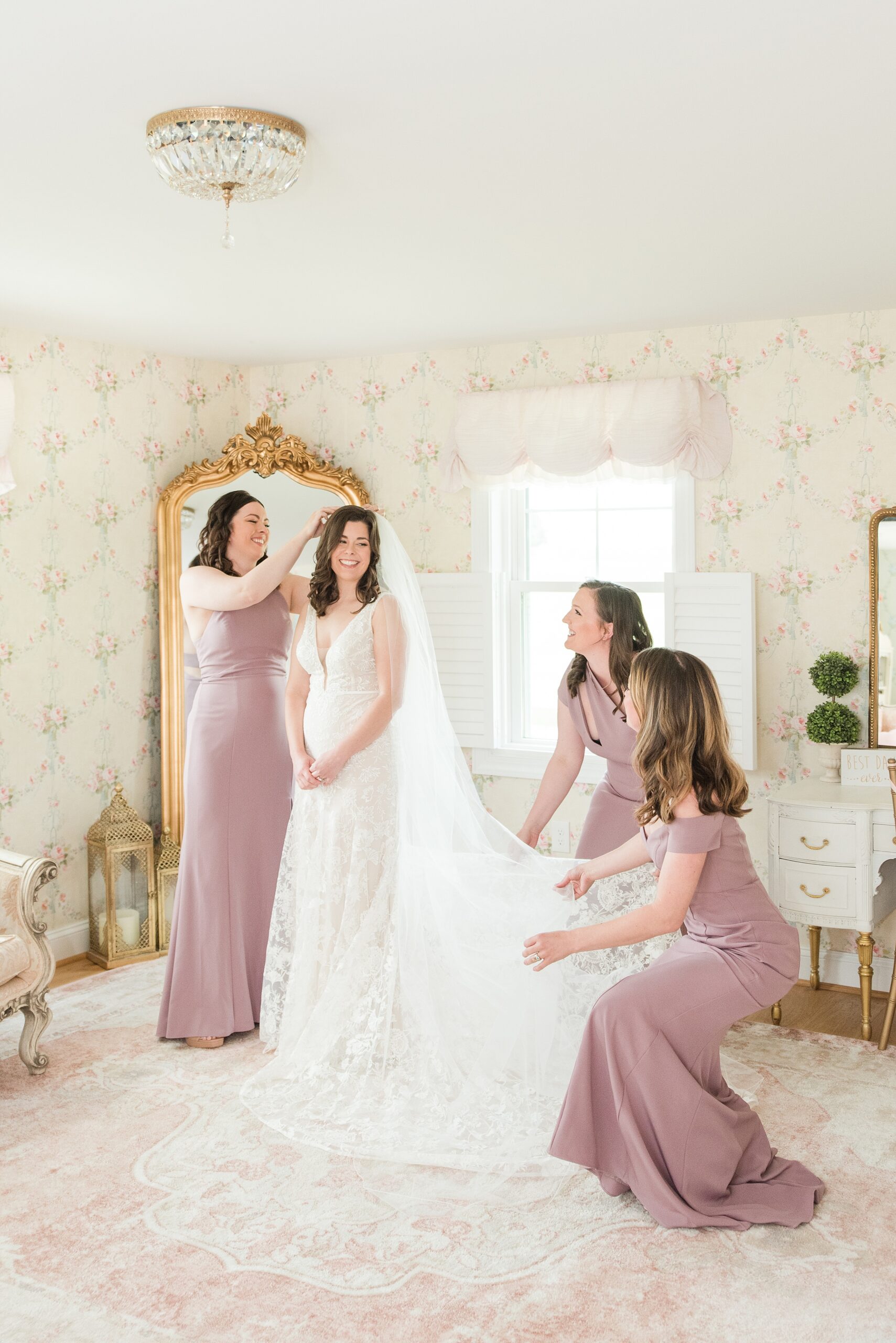 Bridesmaids help the bride put on the finishing touches of her dress and hair before her Bluebird Manor wedding
