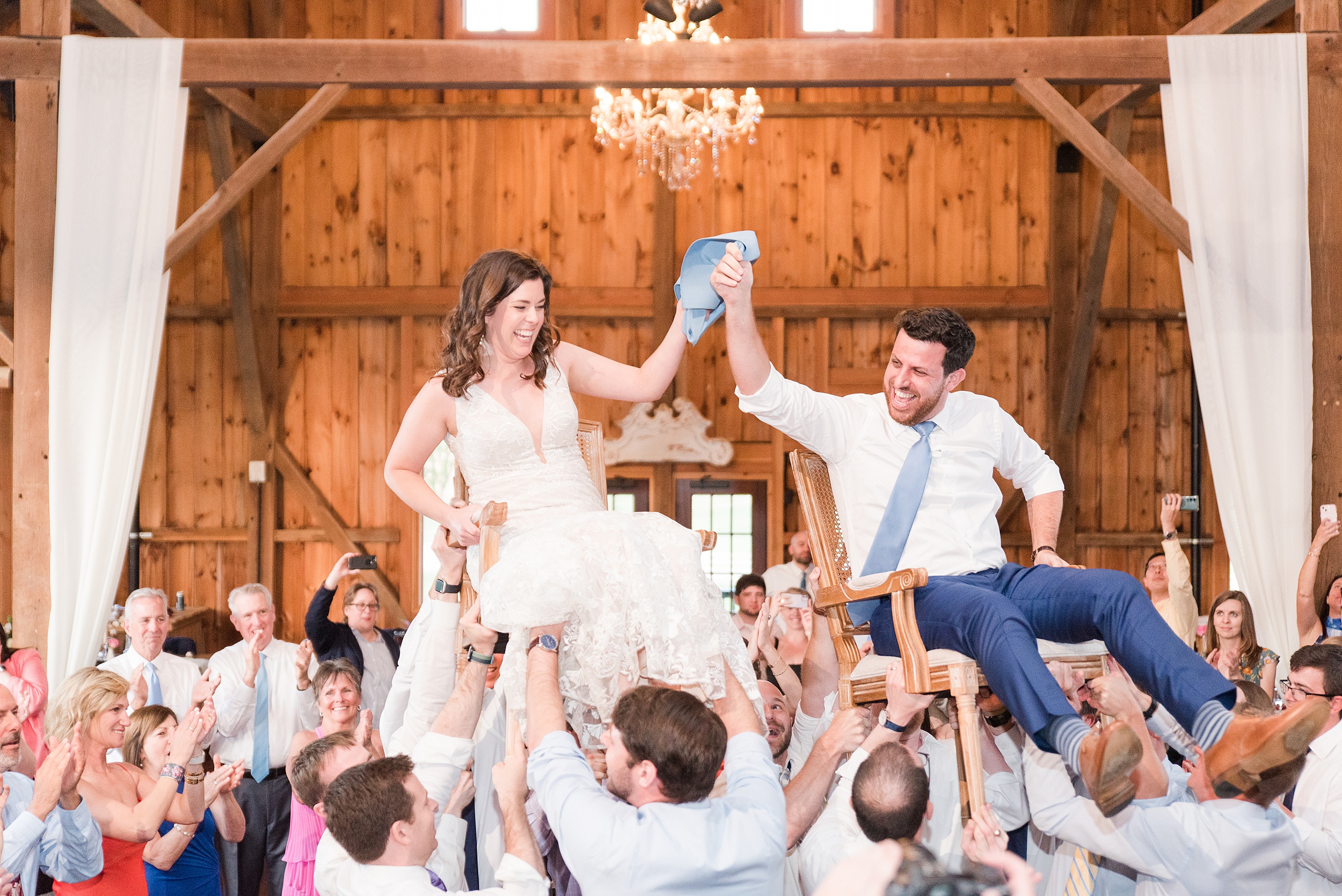 Newlyweds are lifted in wooden chairs on the dance floor during their Bluebird Manor wedding reception