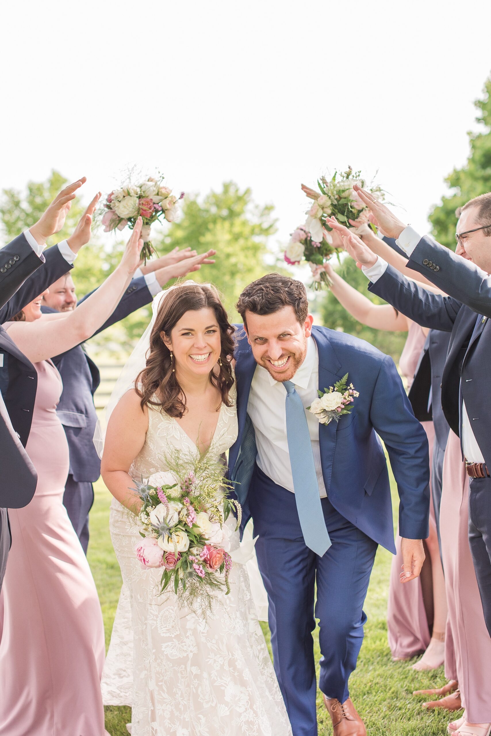 Newlyweds laugh while running under their wedding party's raised hands