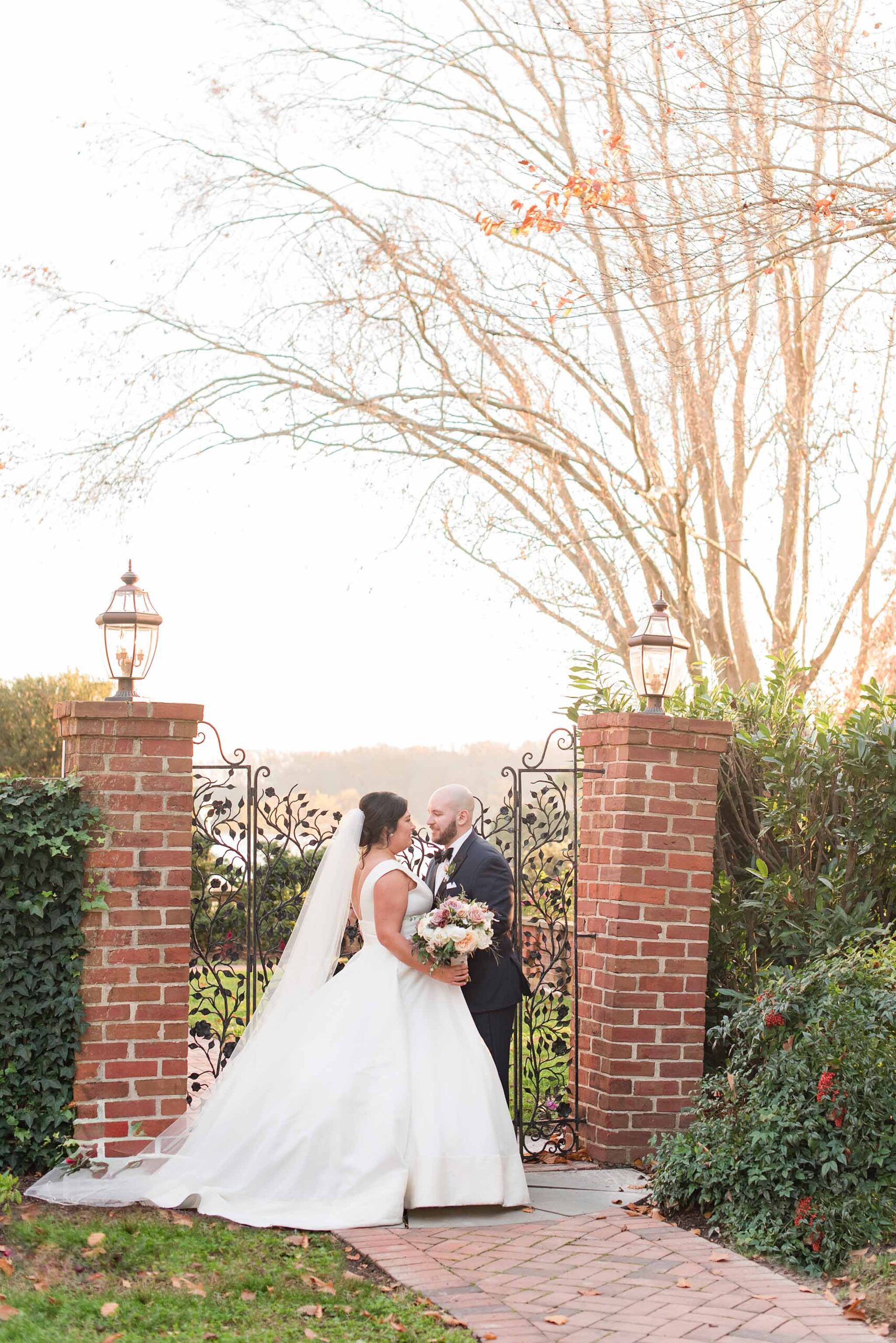 Newlyweds share a quiet sunset moment framed by brick garden walls and iron gate at their Brittland Estates Wedding