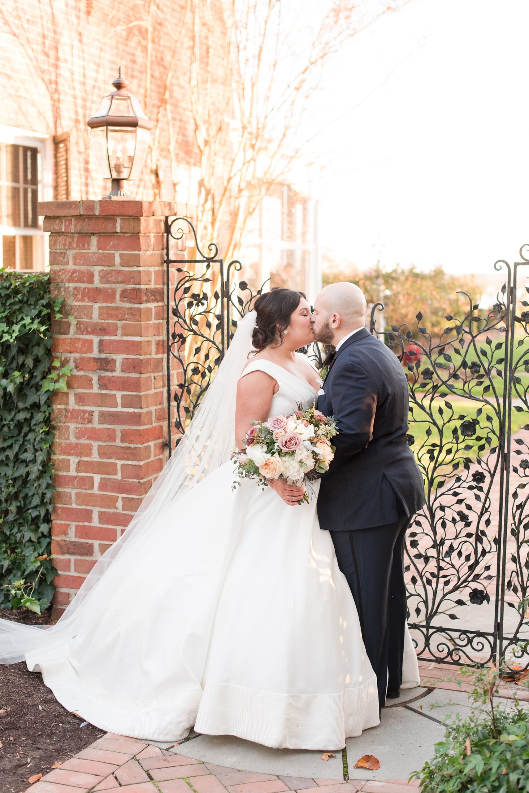 Newlyweds kiss while standing in a garden gate at sunset during their Brittland Estates Wedding