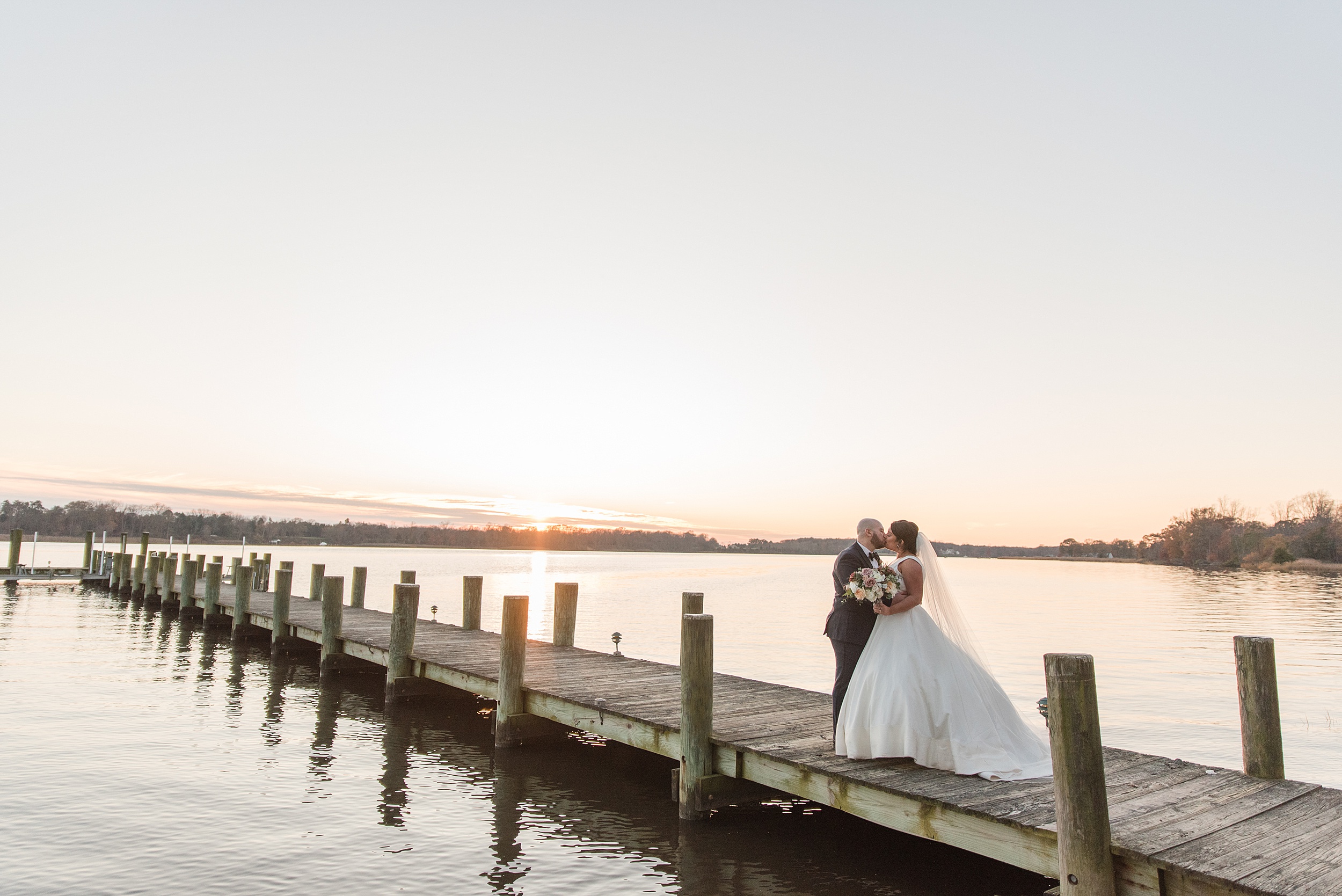 Newlyweds kiss while standing on a long dock at sunset during their Brittland Estates Wedding