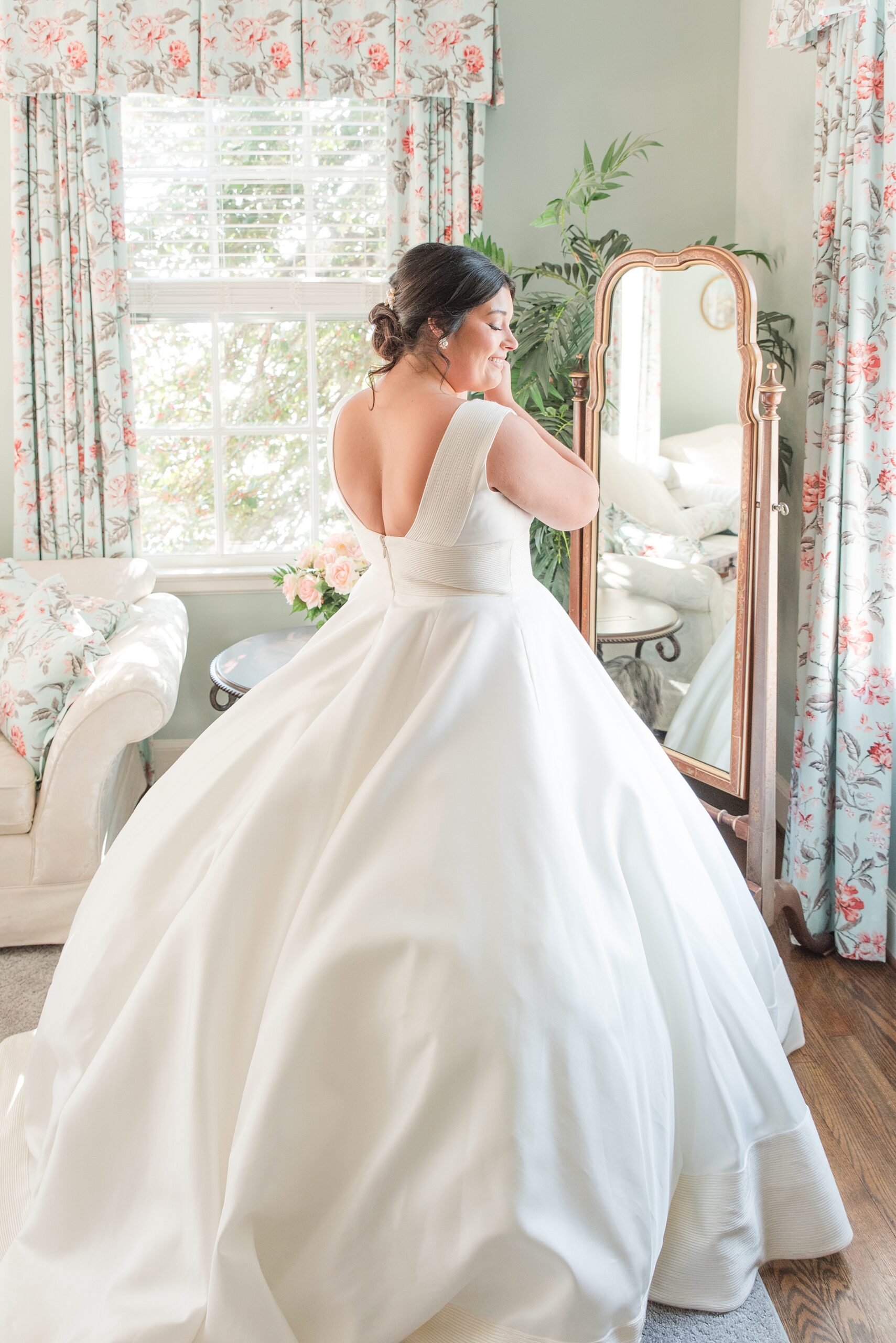 A bride stands in a tall mirror in her dress adjusting an earring