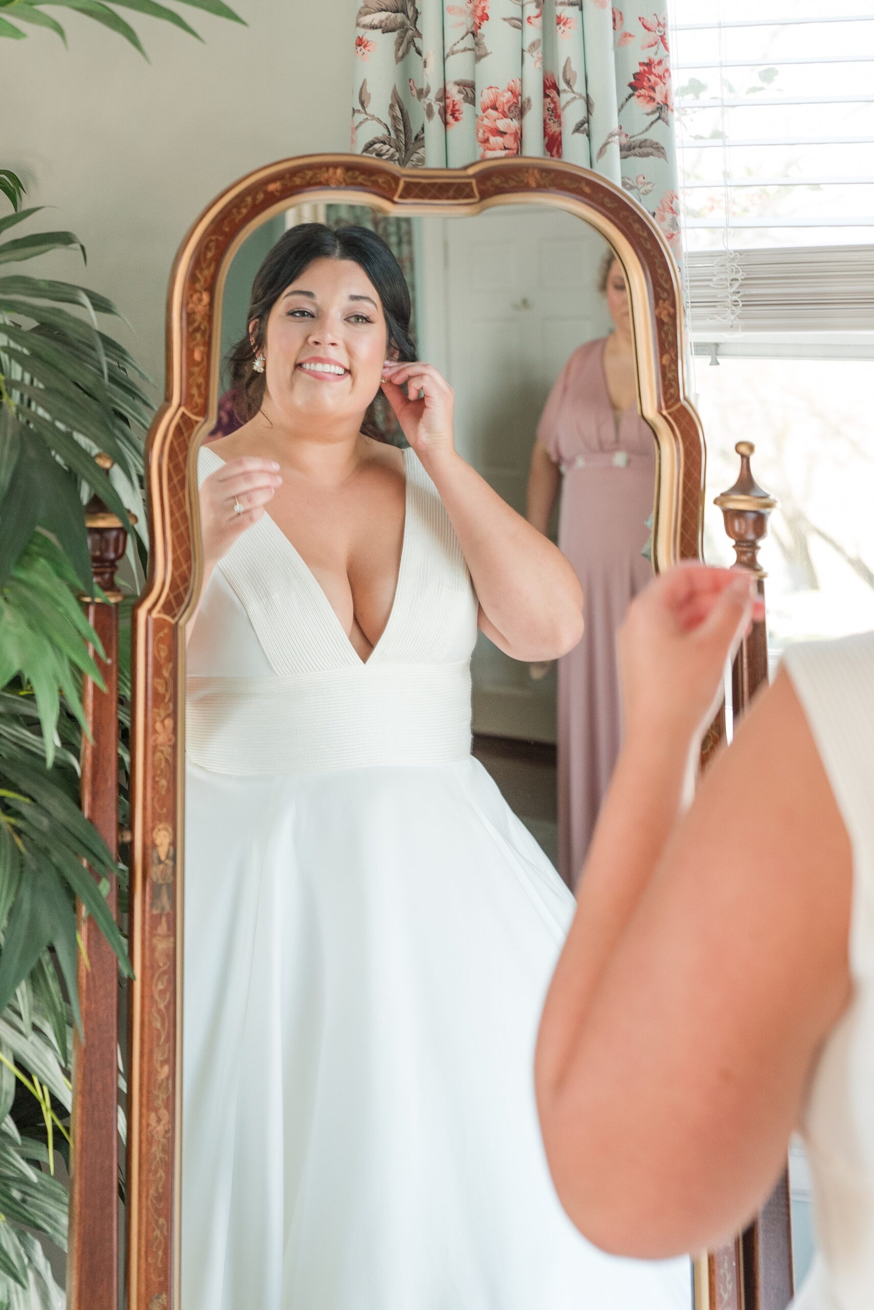 A bride puts on her earrings in a tall mirror