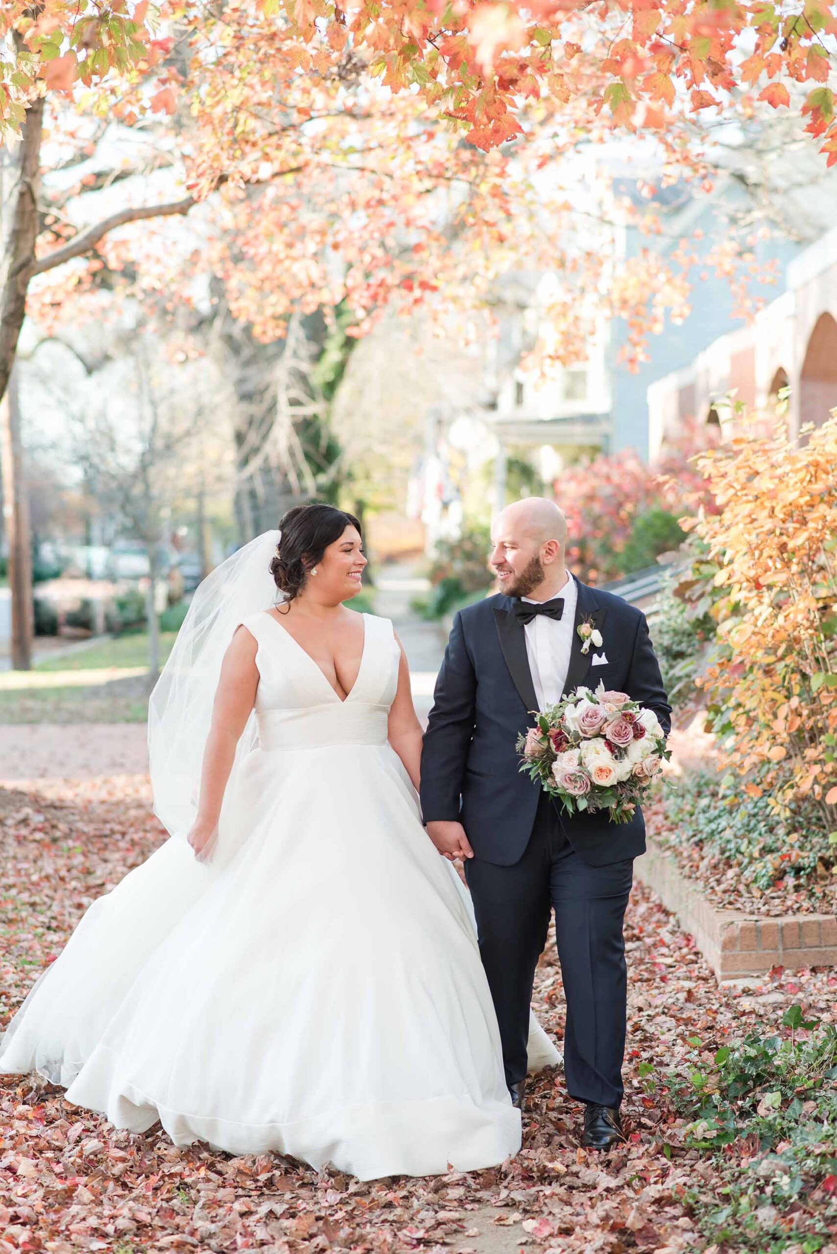 Newlyweds walk down a sidewalk holding hands in fall