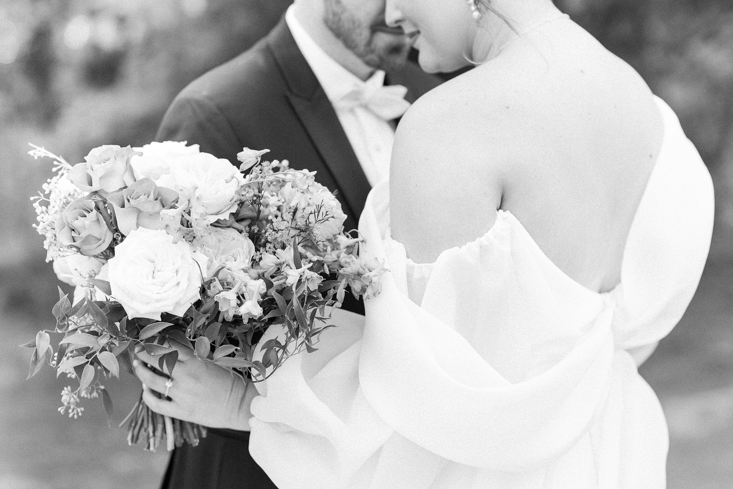 Details of newlyweds snuggling while holding a bouquet outside