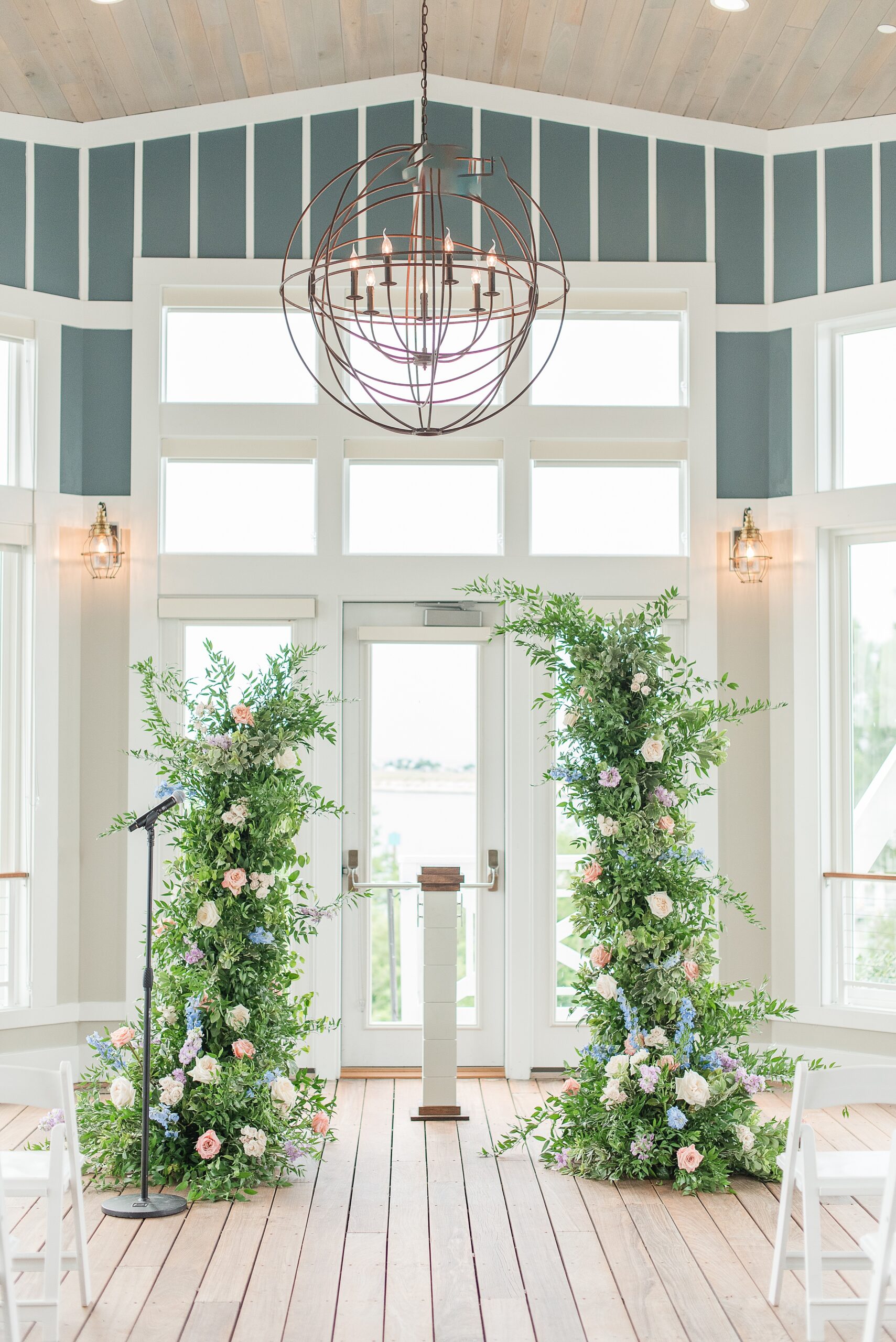 A view of a Chesapeake Bay Beach Club Wedding ceremony altar with floral arches and modern chandelier