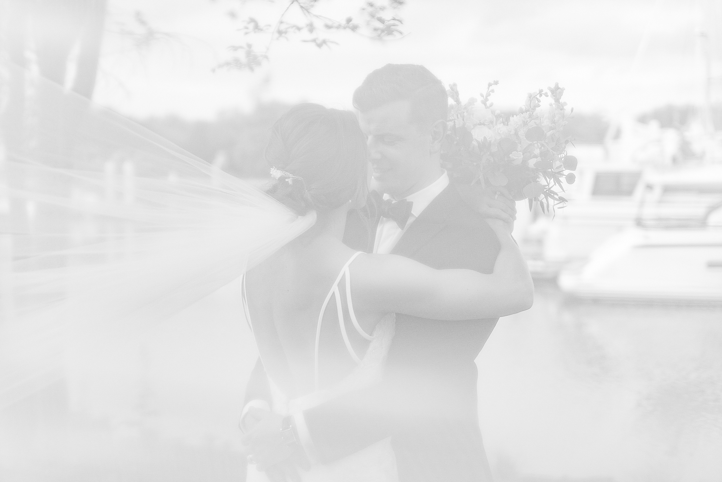 Newlyweds stand by the marina hugging while the veil blows in the wind at their Chesapeake Bay Beach Club Wedding