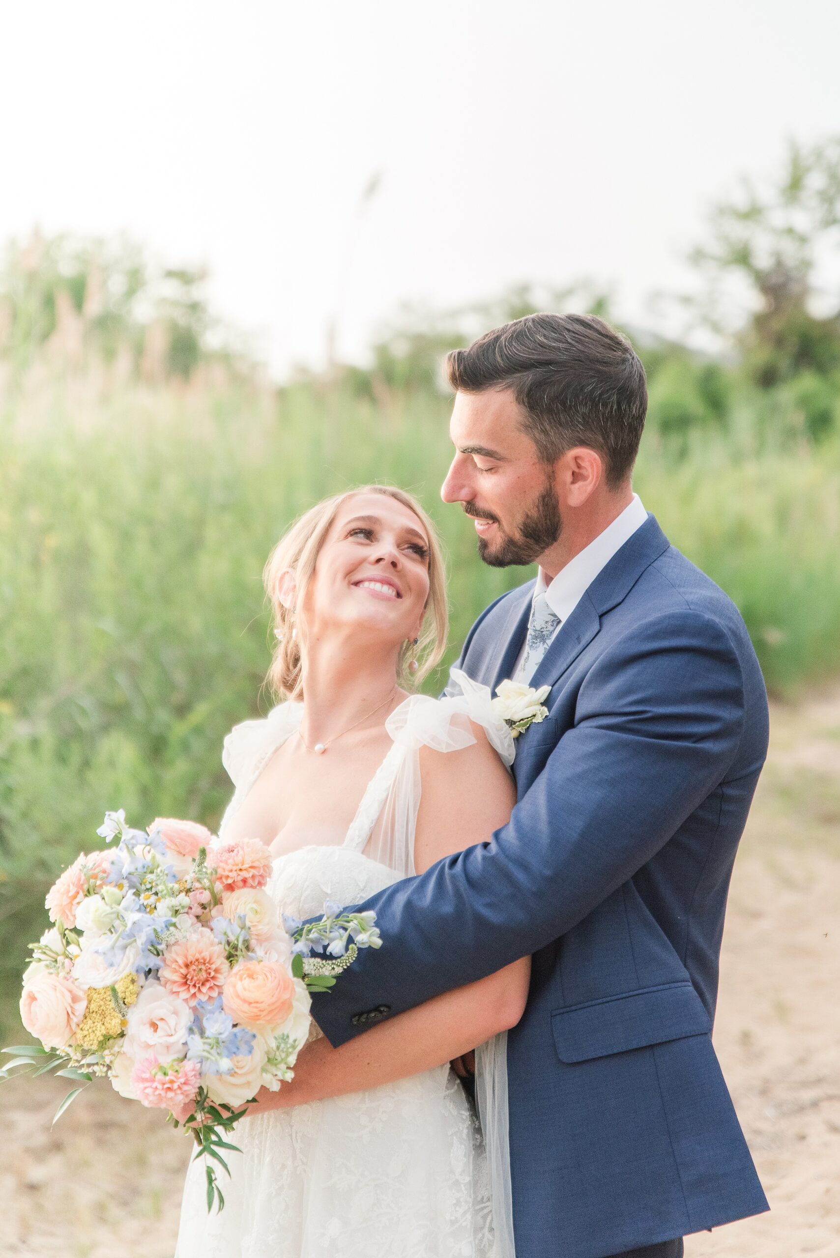 Newlyweds hug and smile at each other while standing in a trail at sunset during their Chesapeake Bay Beach Club Wedding