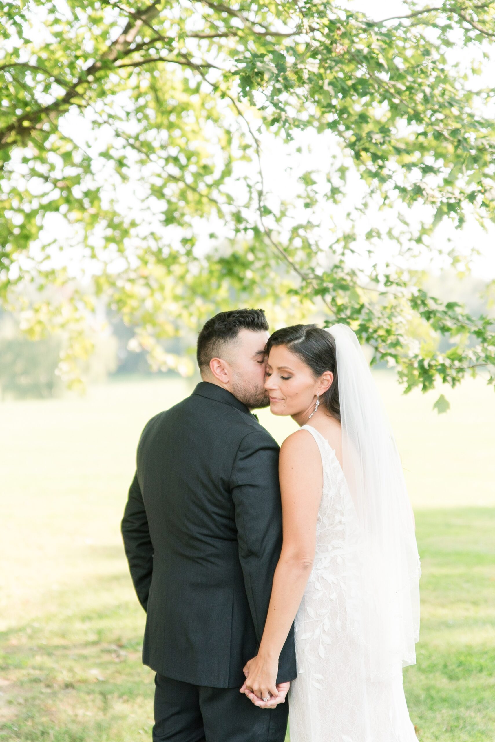 Newlyweds share a kiss and hold hands under a tree at their Historic Oakland Wedding