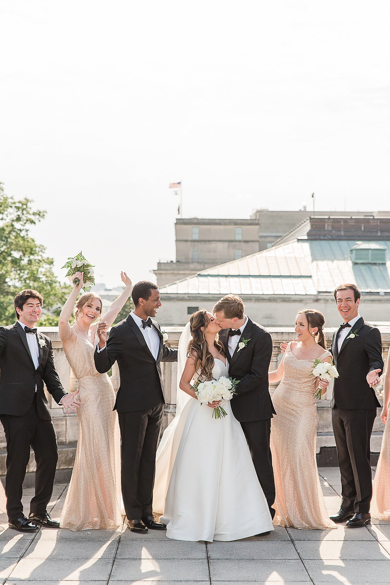 Newlyweds kiss while their wedding party celebrates on a rooftop at one of the Industrial wedding venues Baltimore