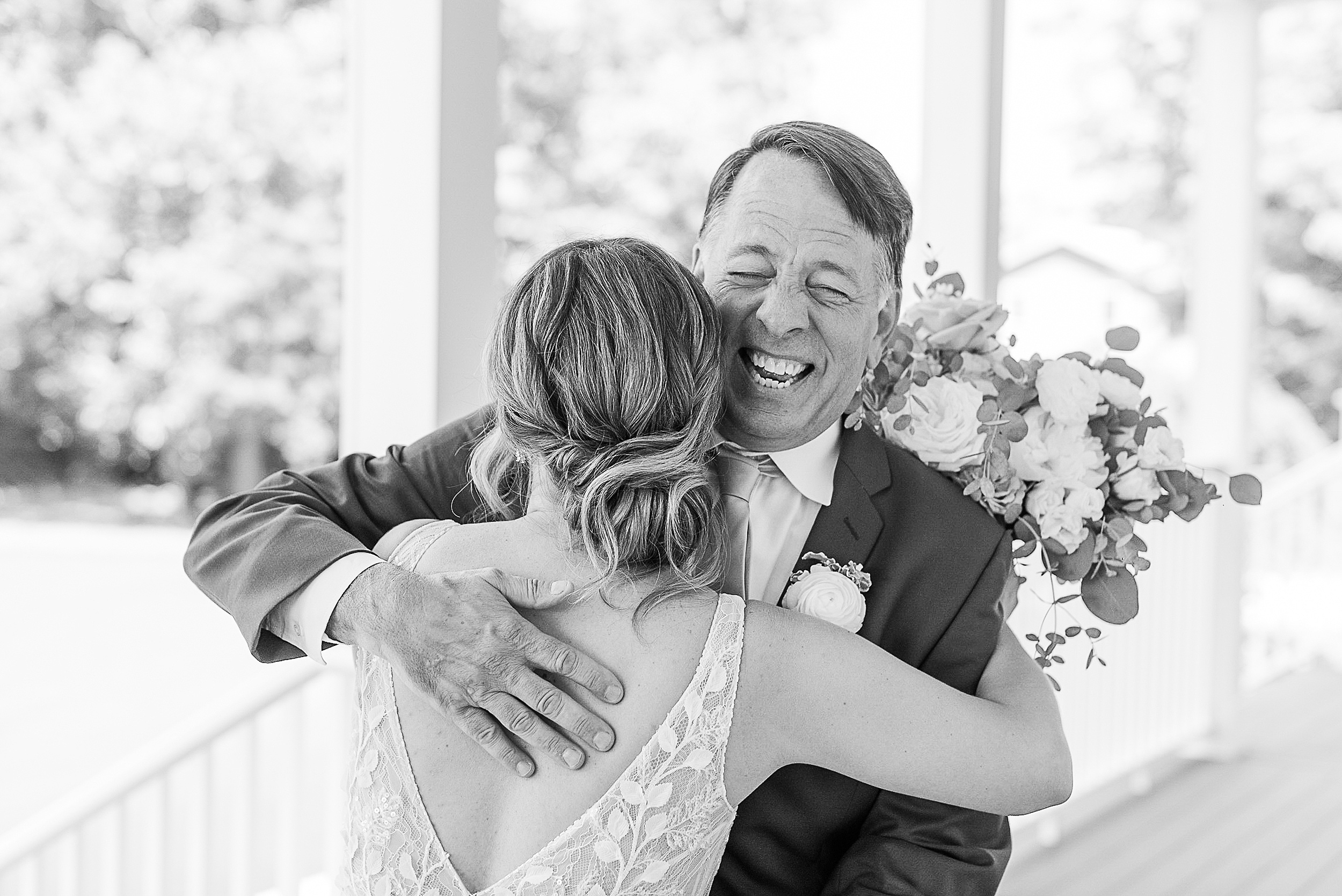 A happy father smiles big while hugging his daughter on her wedding day on a porch