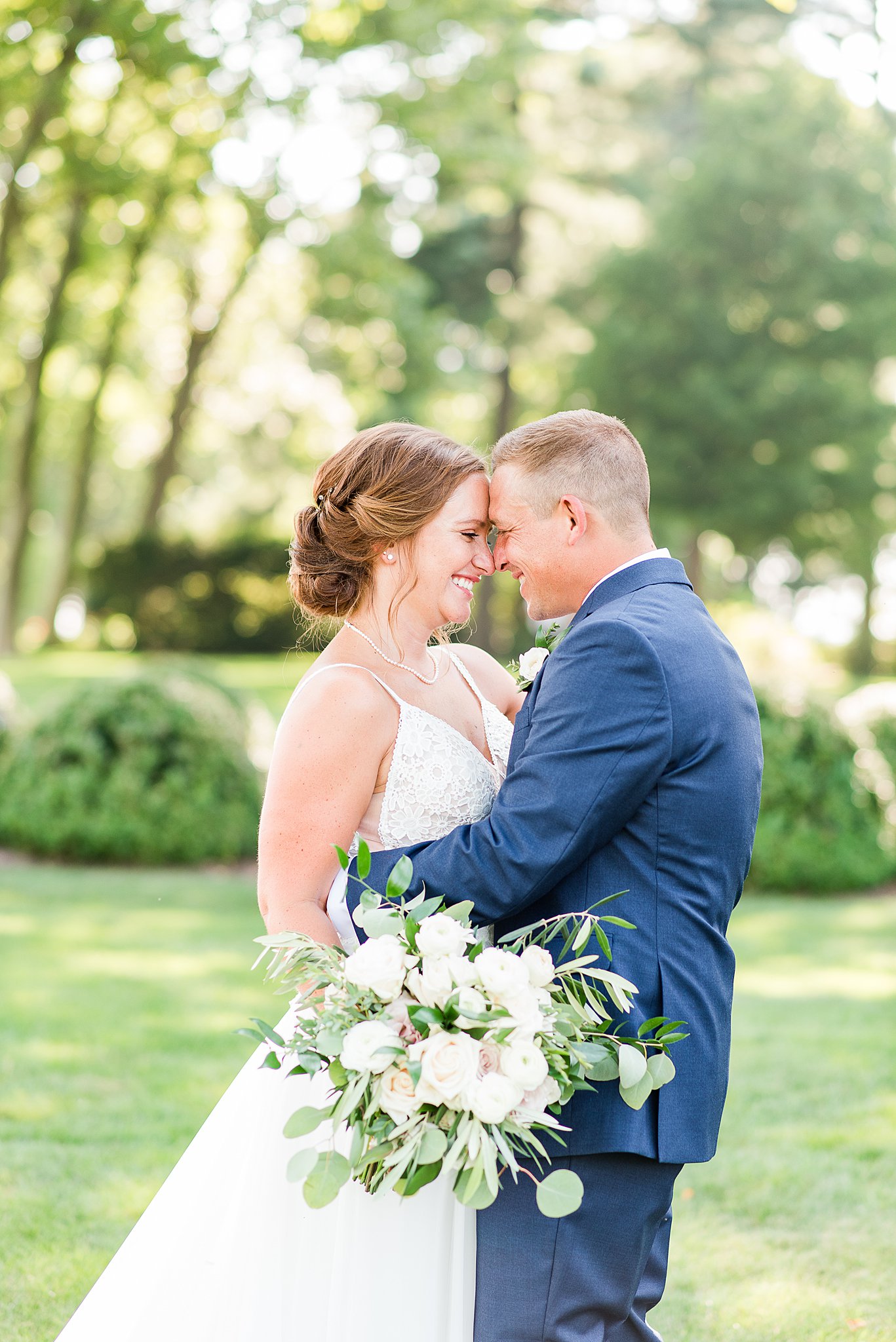 Newlyweds smile big while touching foreheads in a lawn at sunset