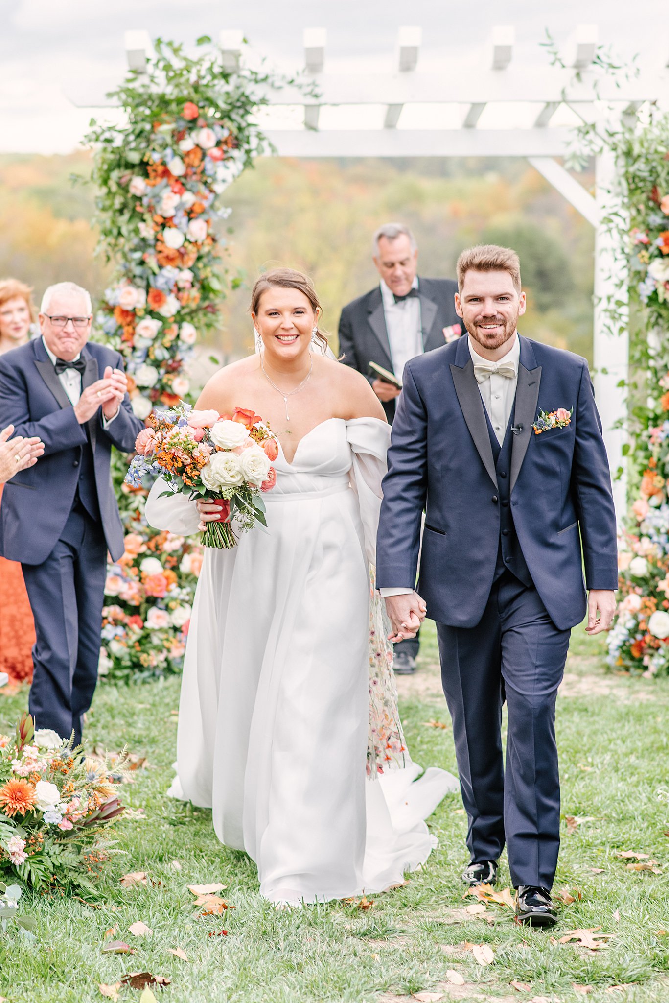 A bride and groom walk back up the aisle holding hands to end their outdoor ceremony