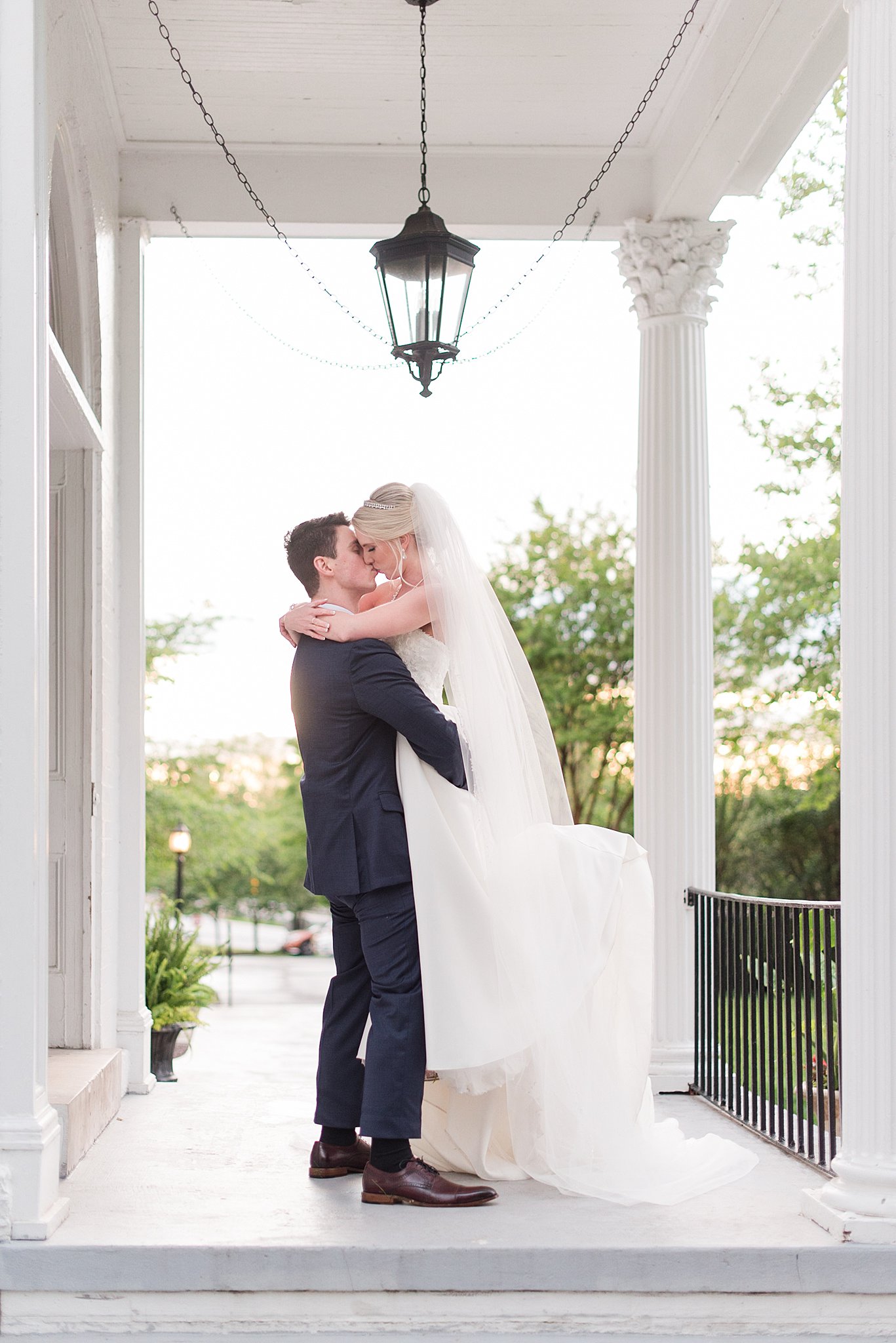 A groom lifts his bride for a kiss while standing on a porch at sunset after using wedding planners Baltimore, MD