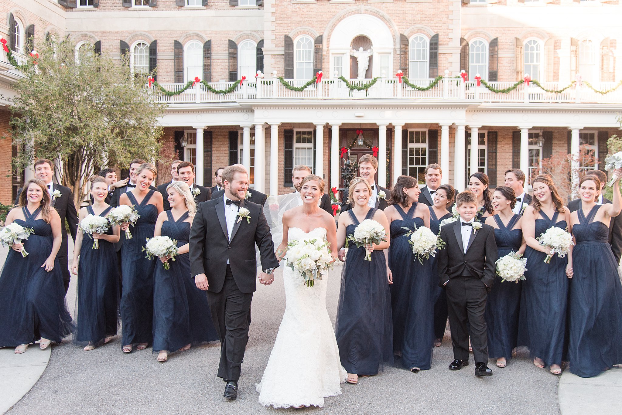 A bride and groom laugh while walking through a courtyard holding hands surrounded by their wedding party thanks to wedding planners Baltimore, MD