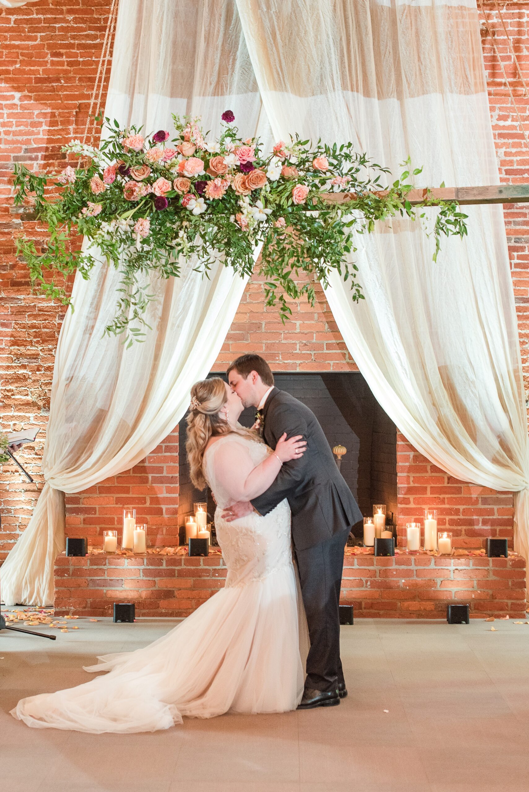 Newlyweds kiss under the wooden arbor in front of the fireplace covered in candles at the Cork Factory Hotel Wedding venue