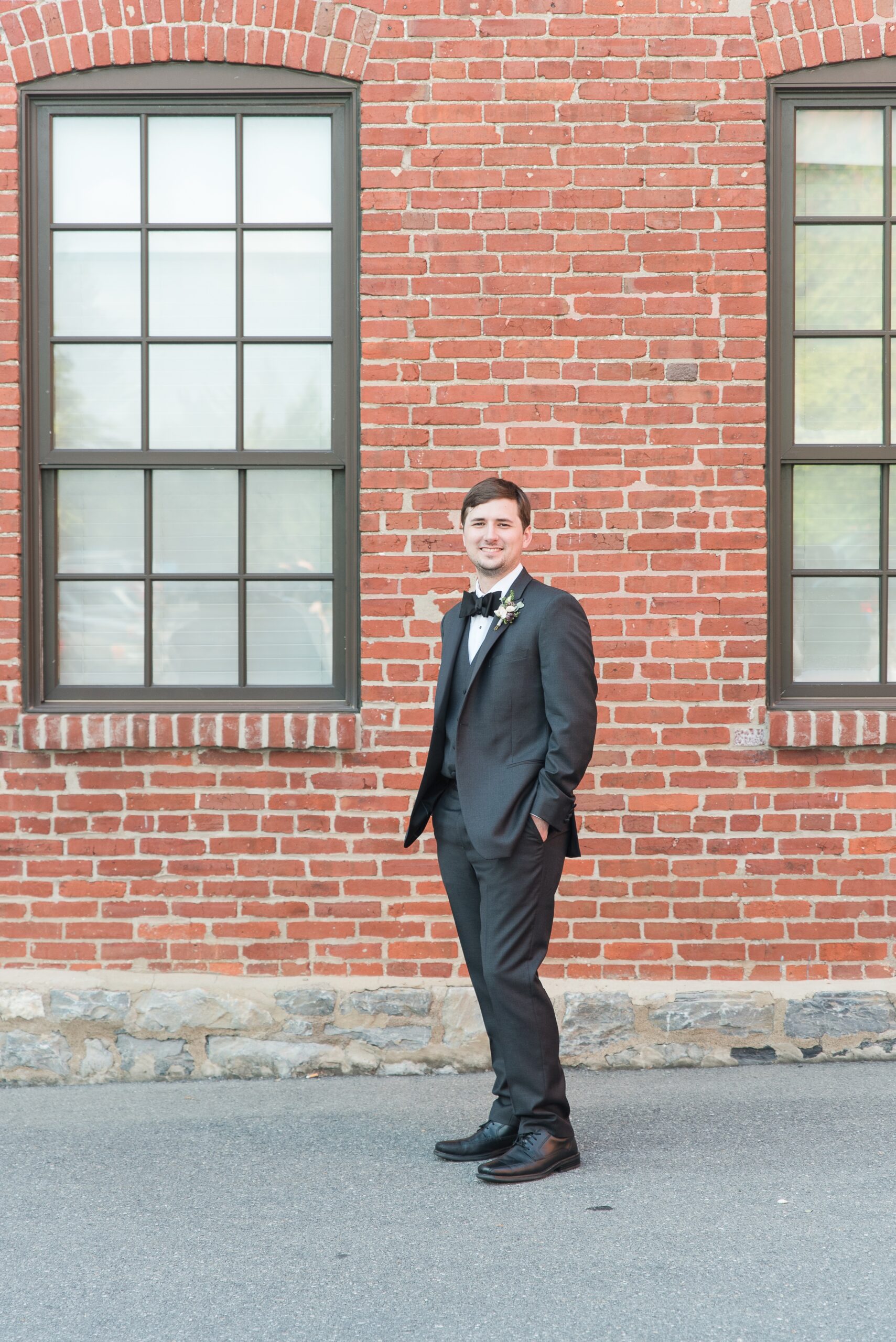 A groom stands against a brick wall in the alley