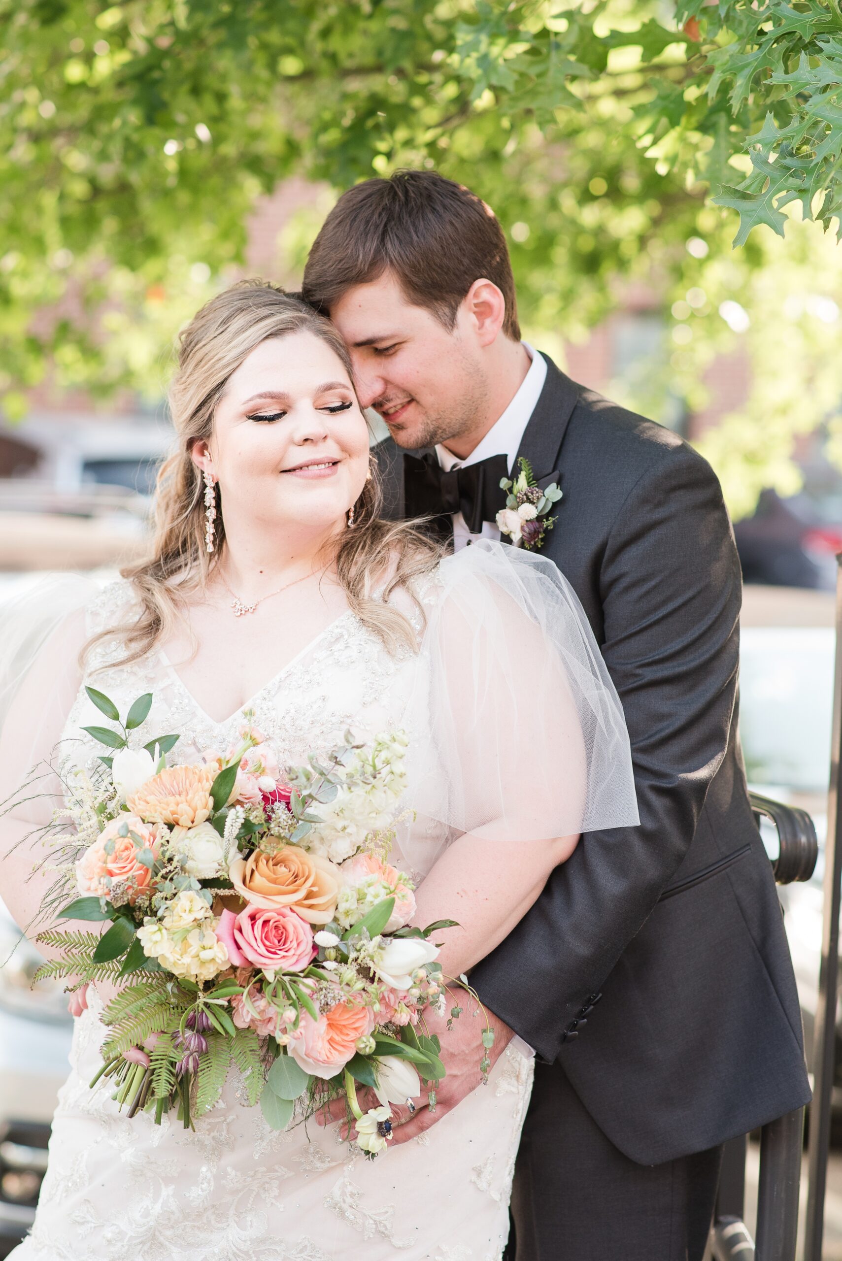 Newlyweds stand under a tree while snuggling