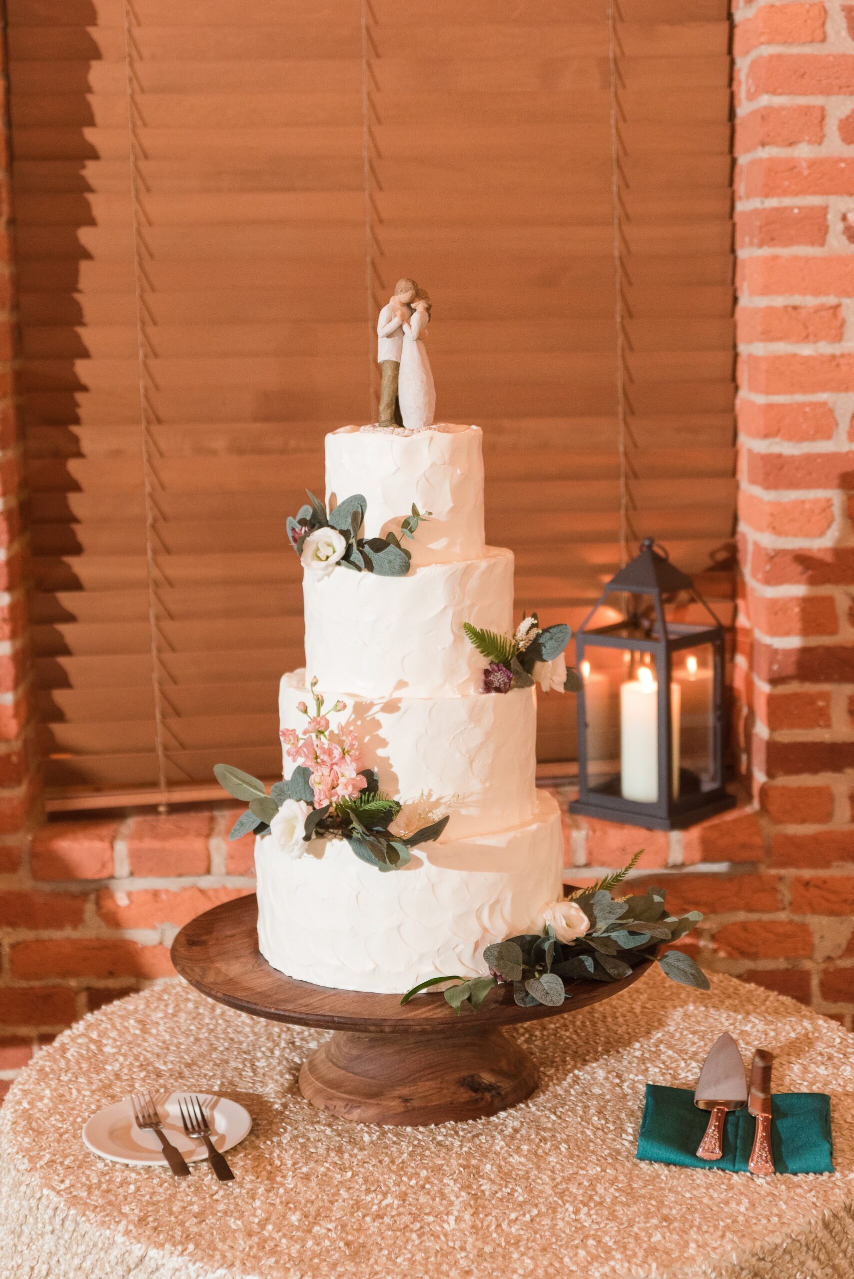 Details of a four tier wedding cake on a wooden stand with flowers and dancing topper