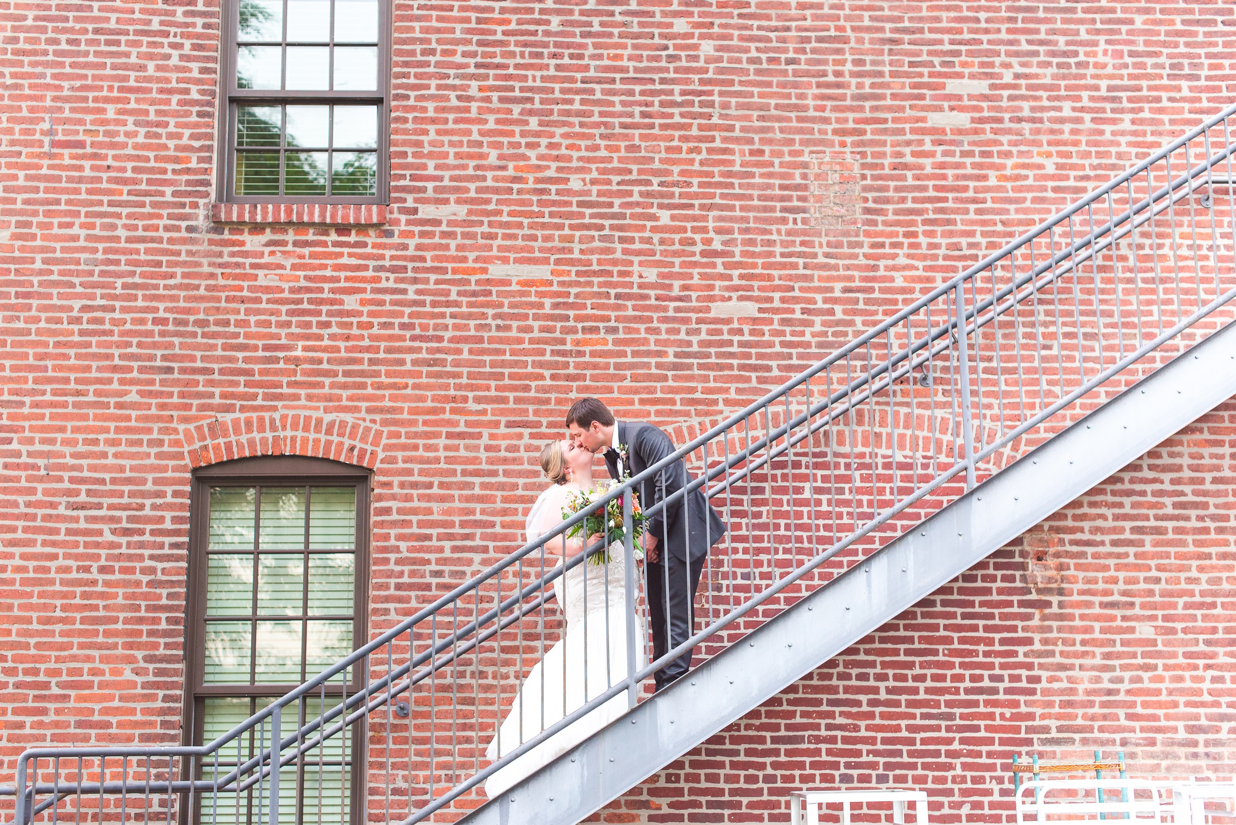 Newlyweds kiss on metal stairs against a brick wall at the Cork Factory Hotel Wedding venue