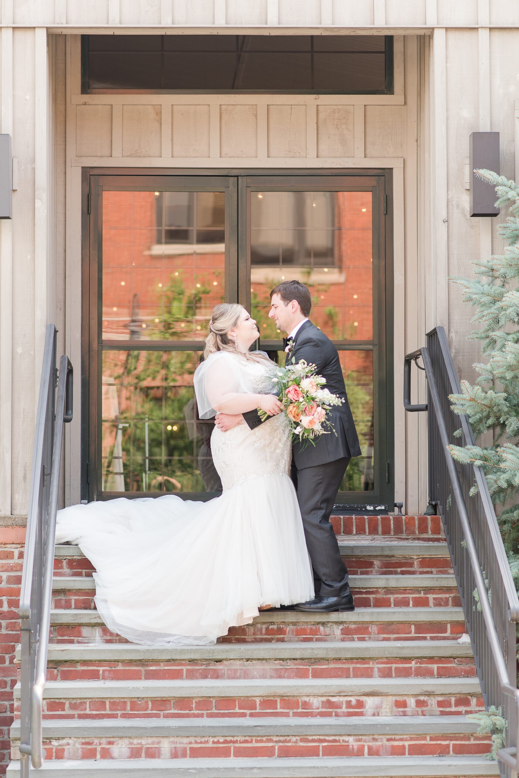 Newlyweds share a hug and lean in for a kiss while standing on brick stairs