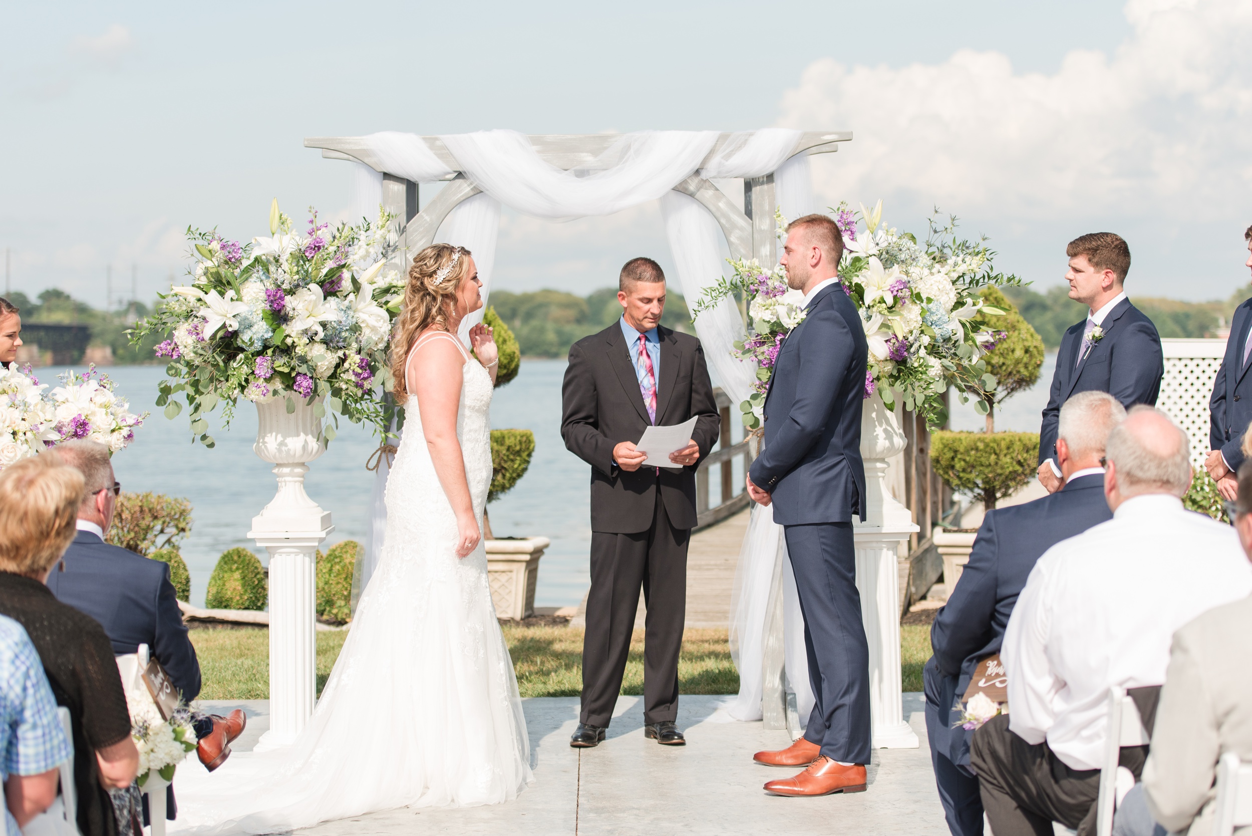 A bride and groom stand at their outdoor arbor La Banque de Fleuve Wedding ceremony