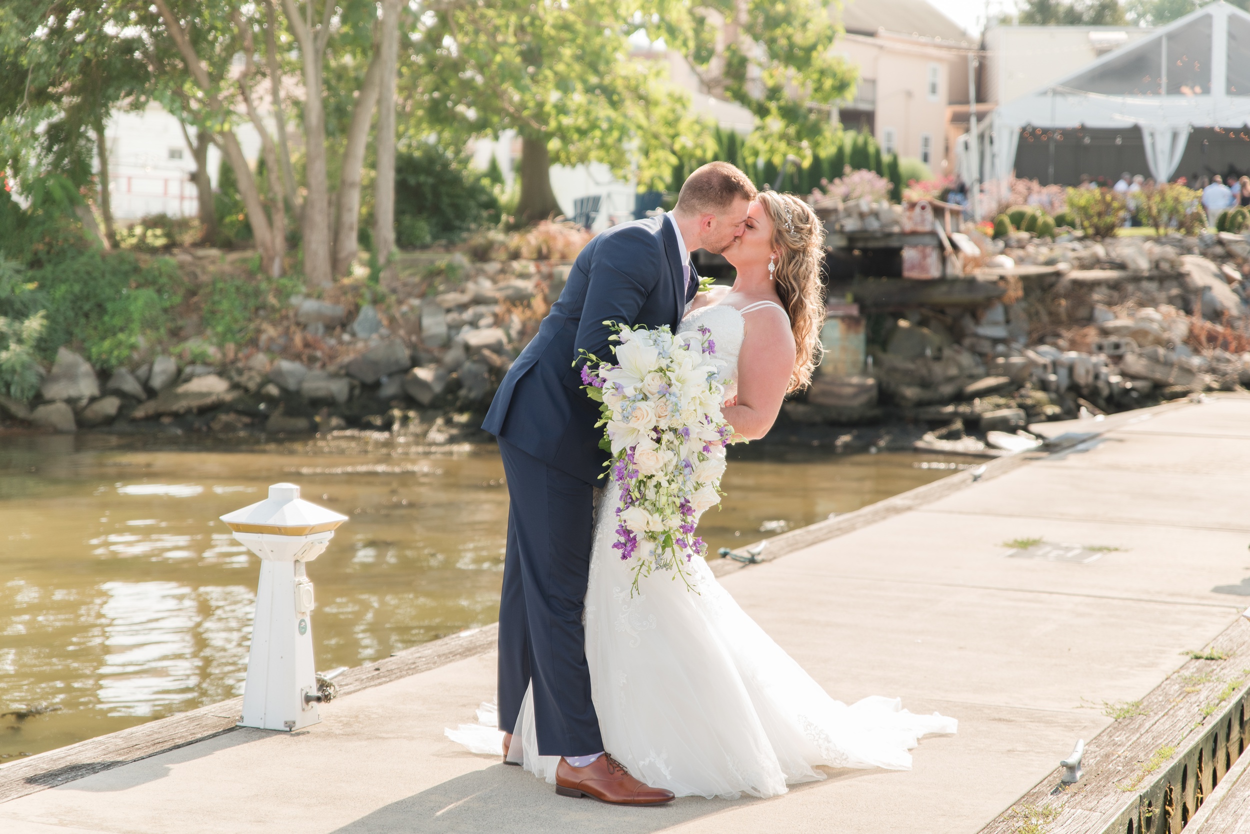 A groom dips his bride while kissing her on a floating dock