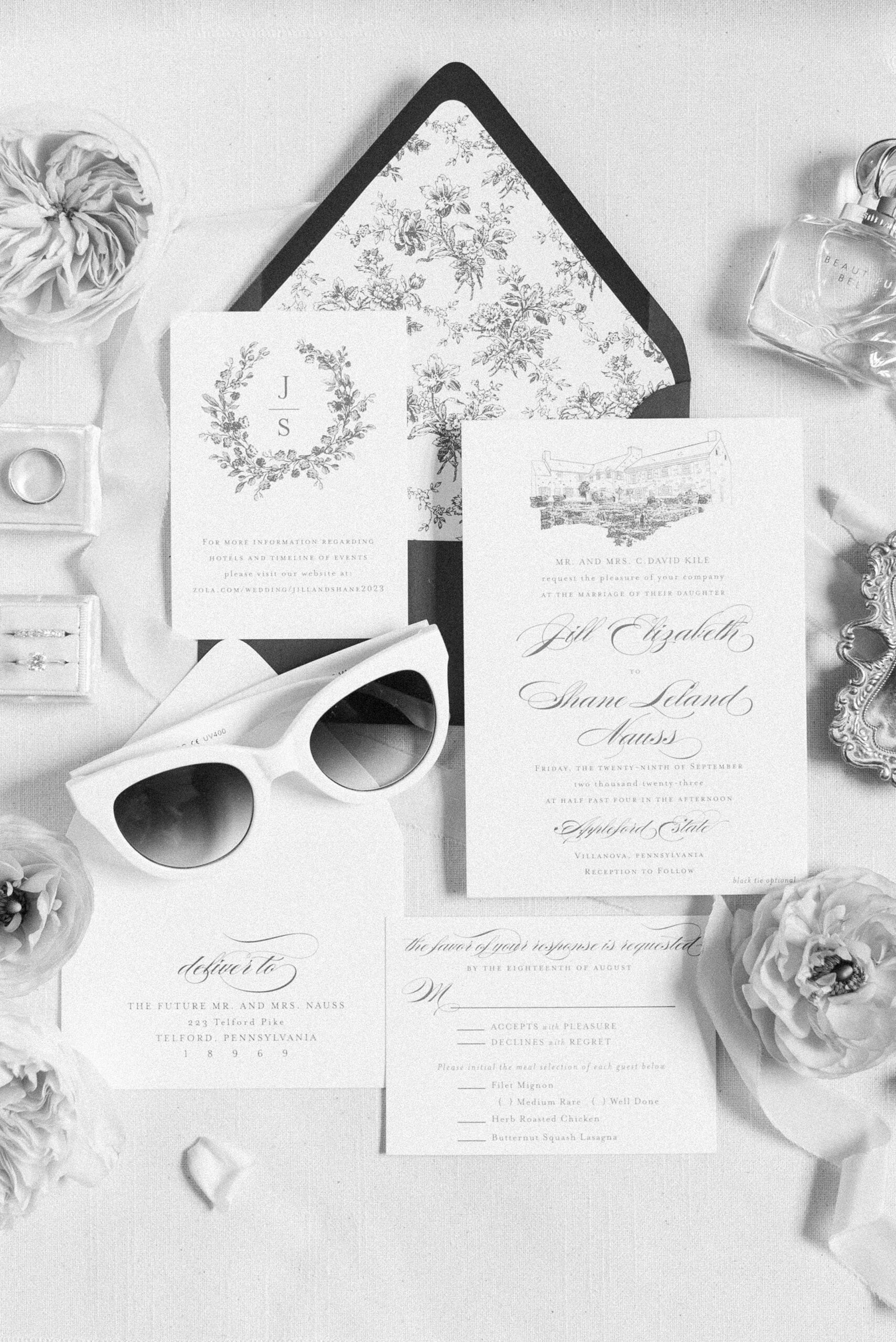 Bridal details including invitations and sunglasses sit on a table with flowers