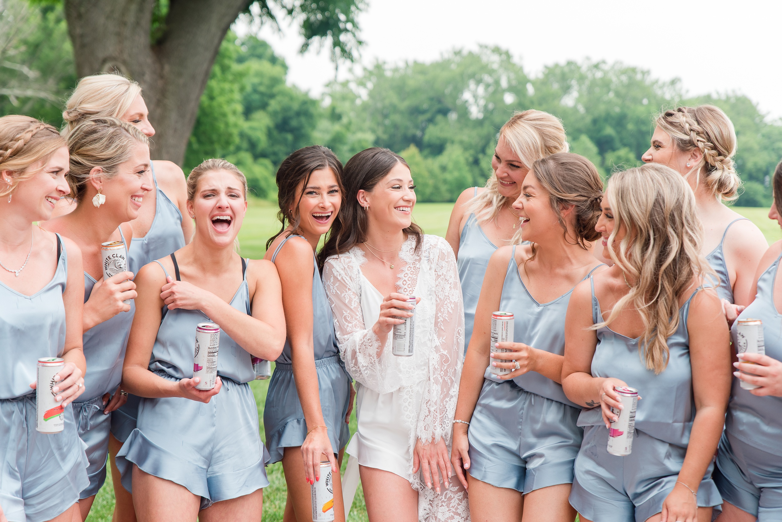 A bride laughs with her many bridesmaids in pajamas while drinking white claws at her Swan Harbor Farm Wedding
