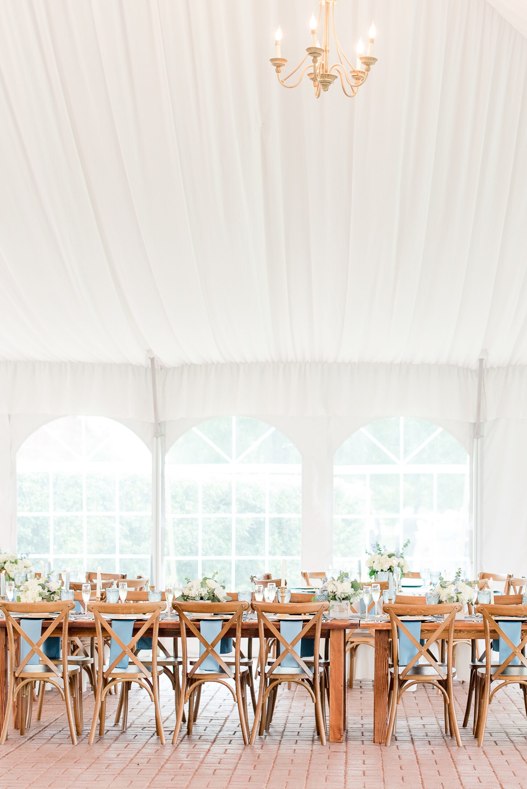 Details of a tent wedding with wooden tables and chairs and a high chandelier at a Swan Harbor Farm Wedding