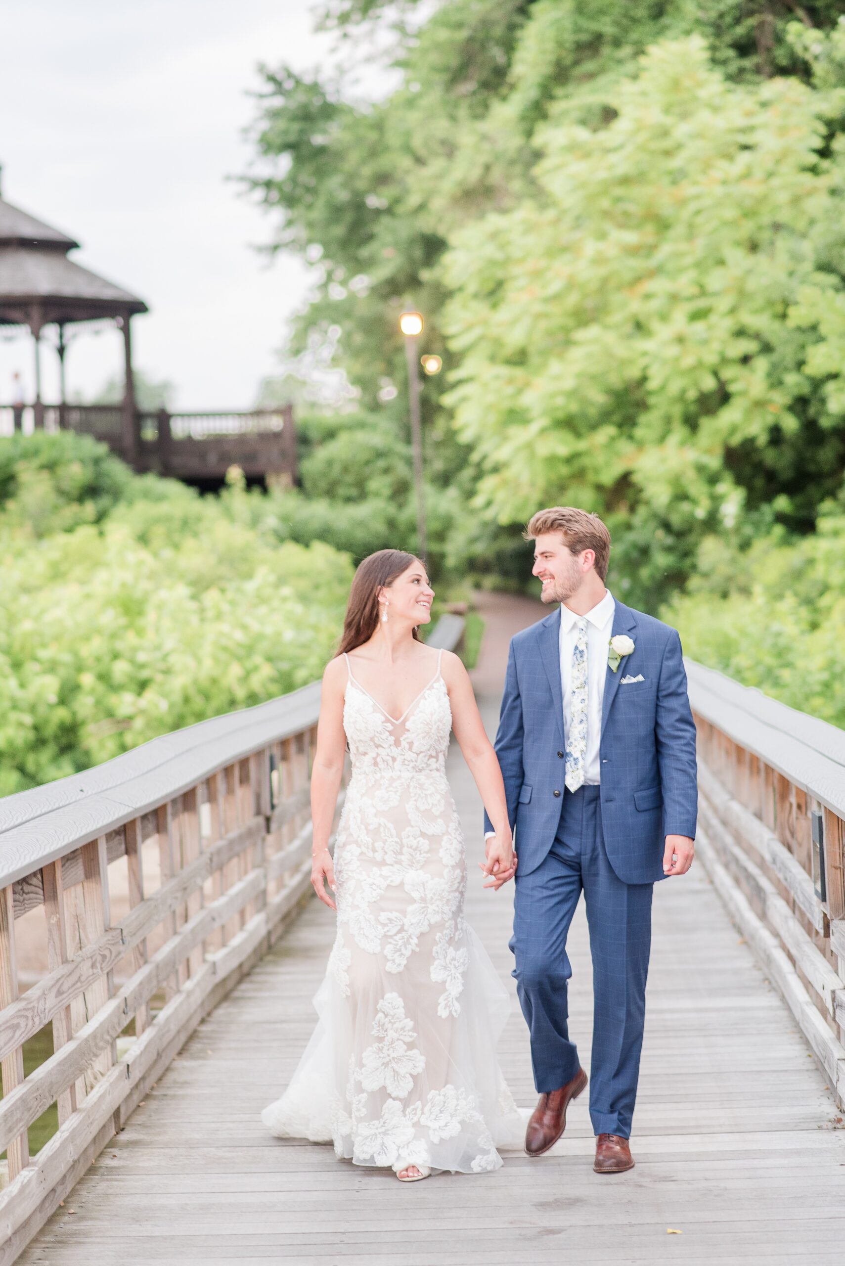 Newlyweds walk hand in hand down a boardwalk while smiling at each other at their Swan Harbor Farm Wedding