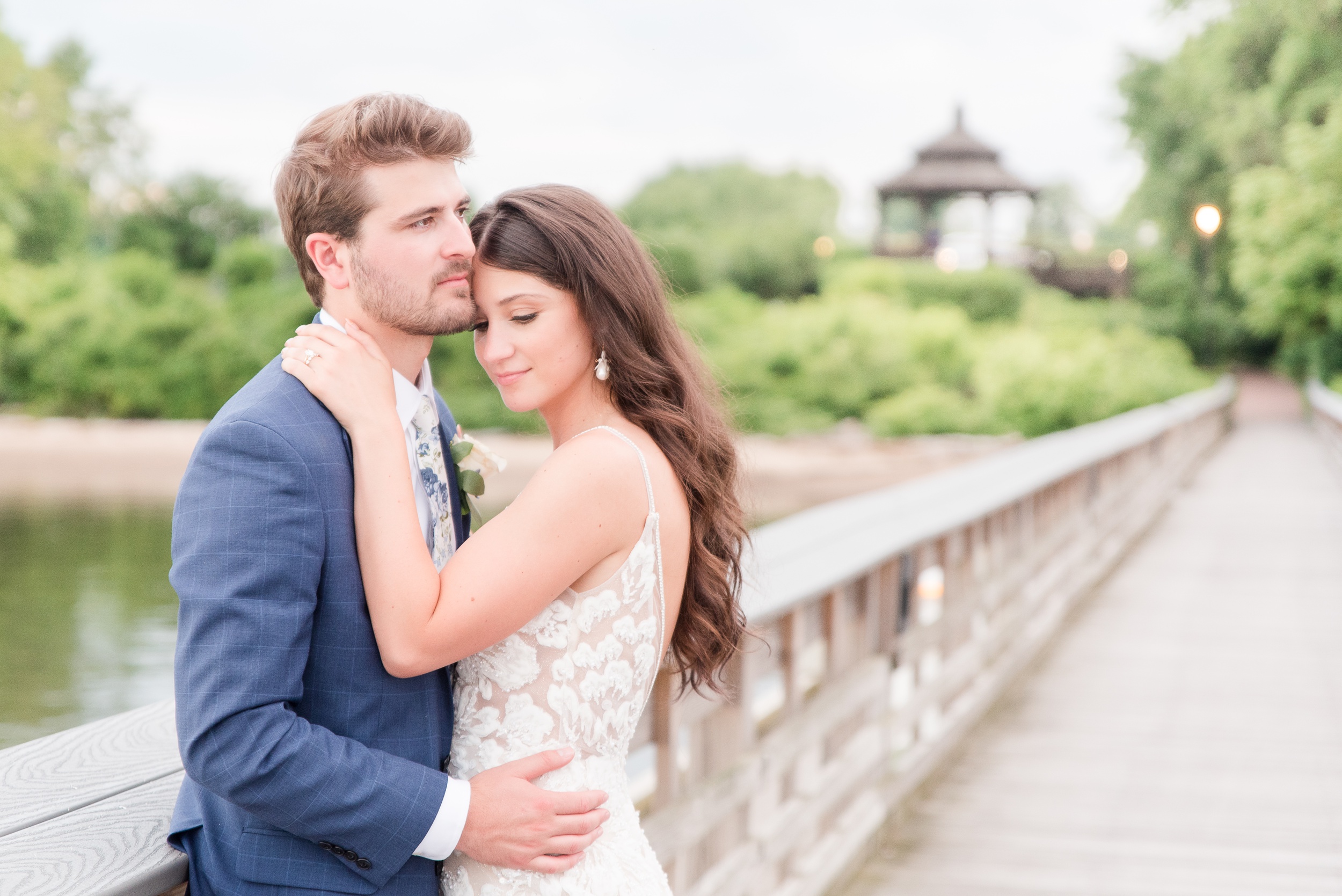 A bride snuggles on her groom as they lean on a boardwalk railing at their Swan Harbor Farm Wedding
