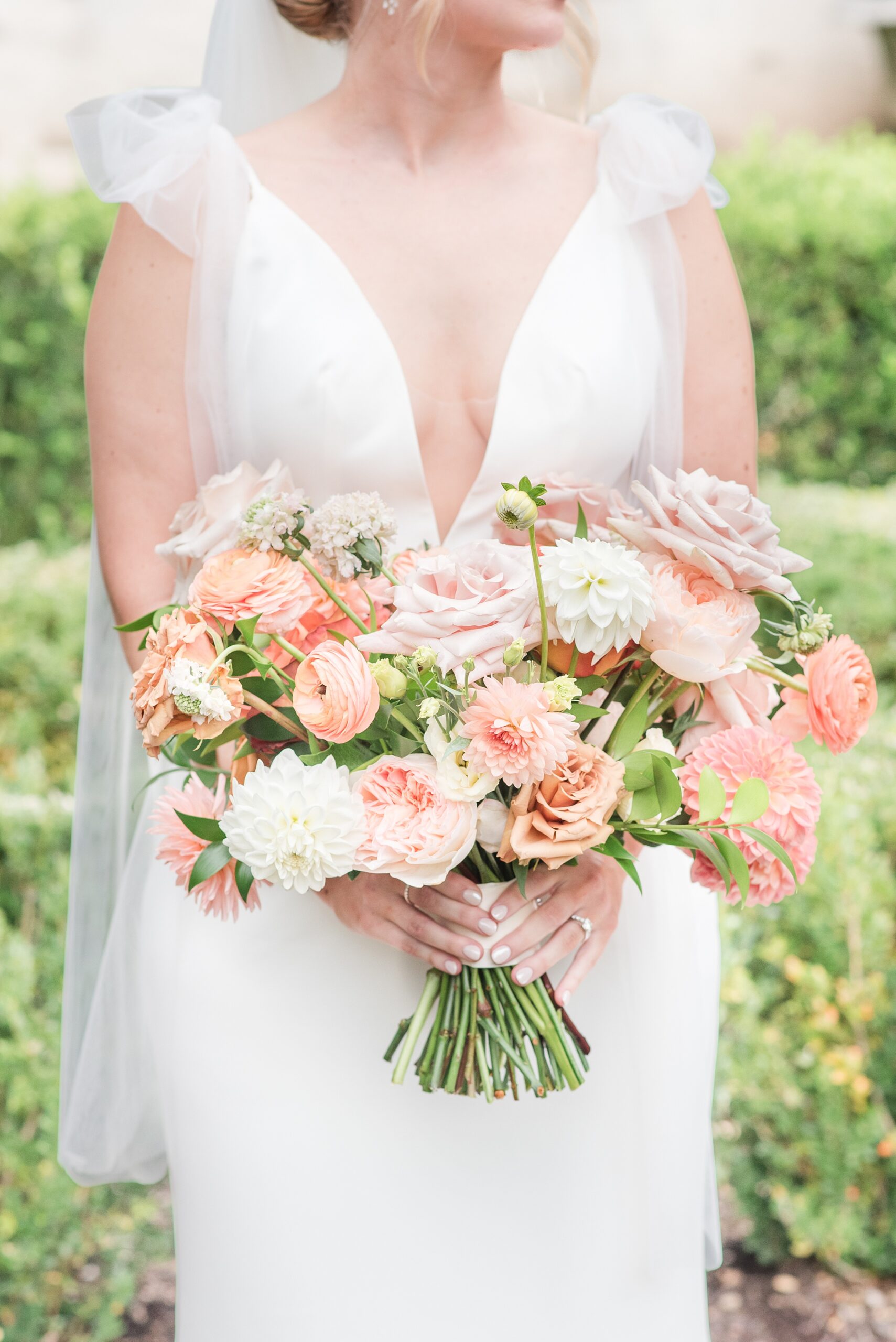 Details of a bride in a silk dress with long veil standing in a garden holding her bright pink bouquet at her Annapolis Waterfront Hotel Wedding