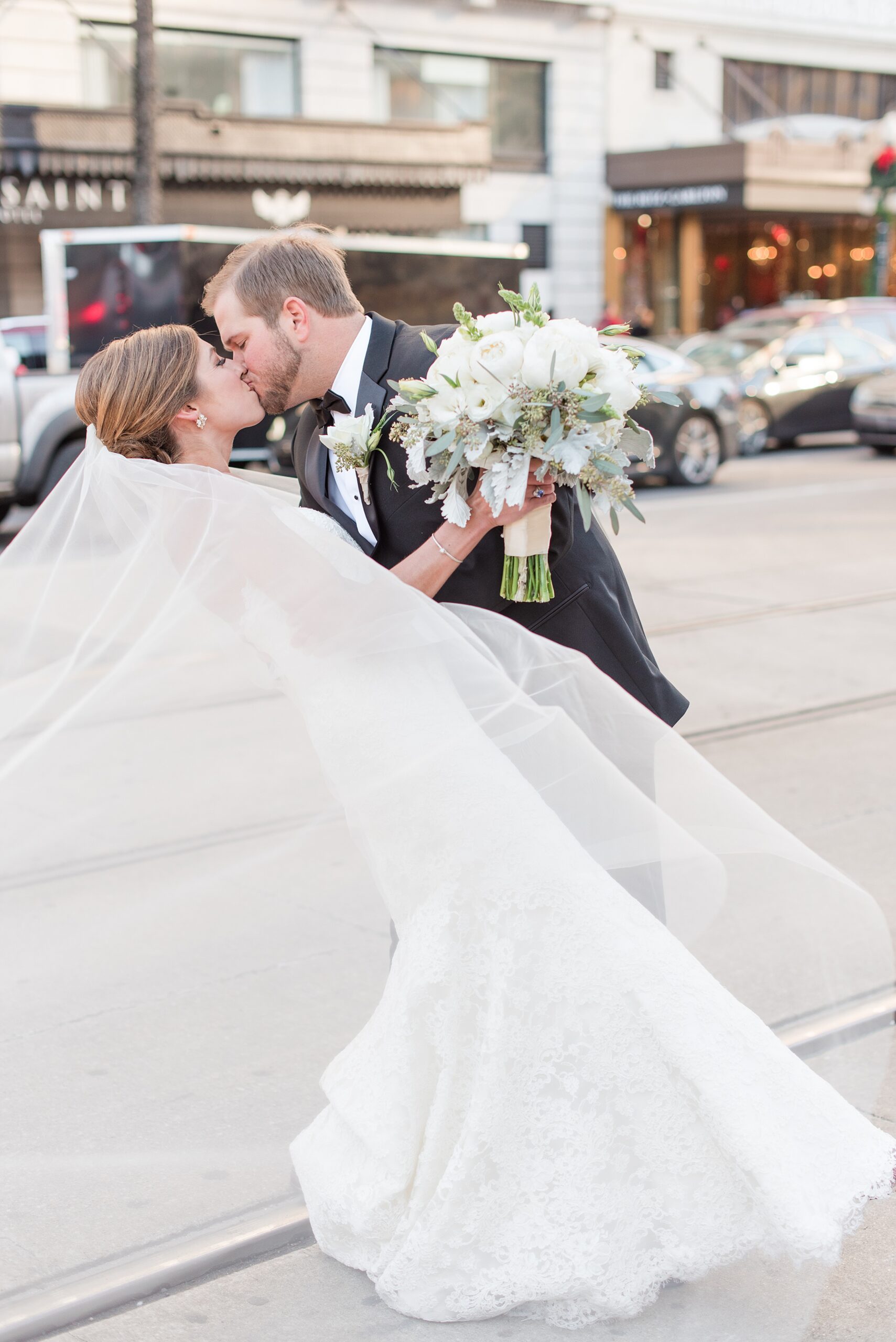 Newlyweds kiss on the street while the veil blows in the wind