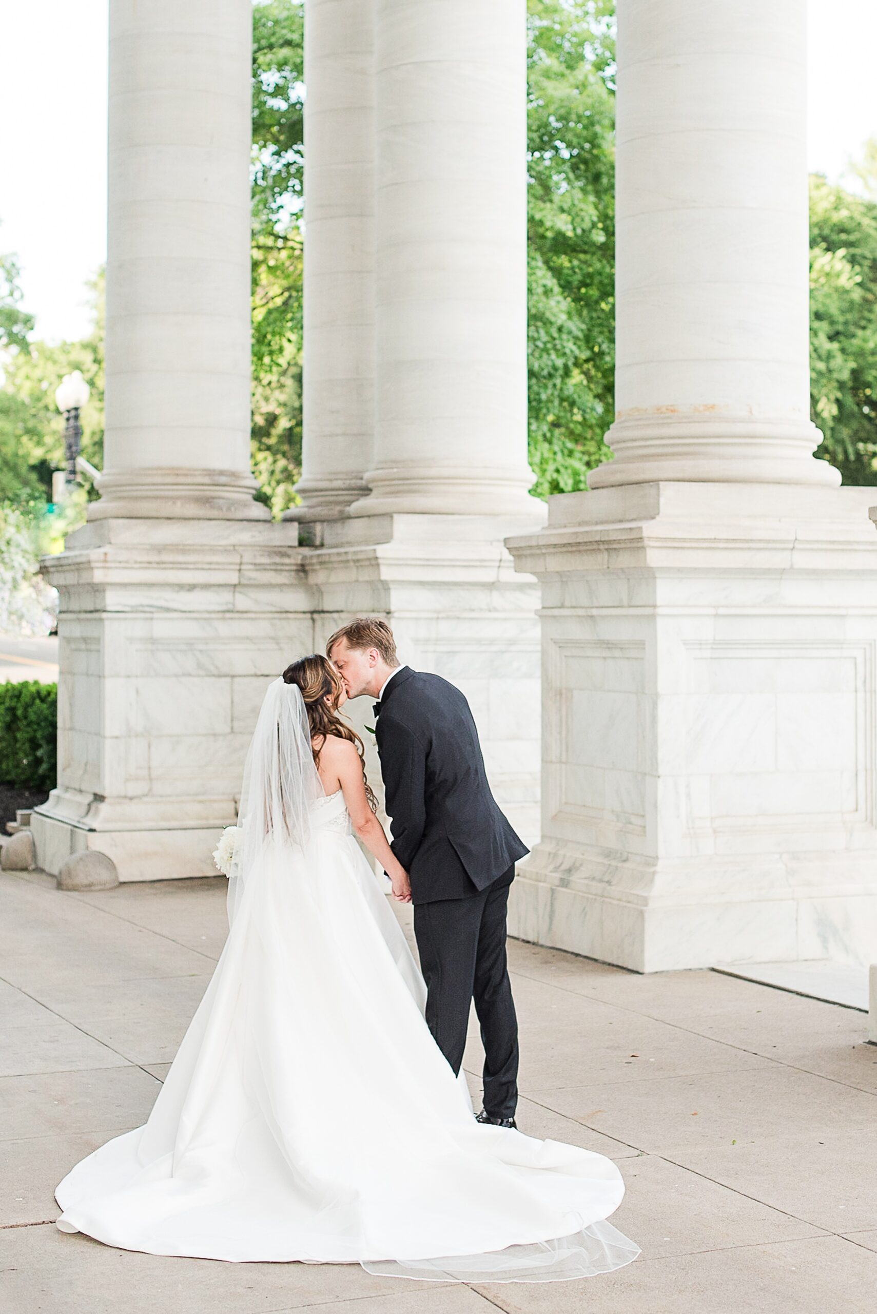 Newlyweds kiss while holding hands and walking through a colonial porch at their Army Navy Club Wedding