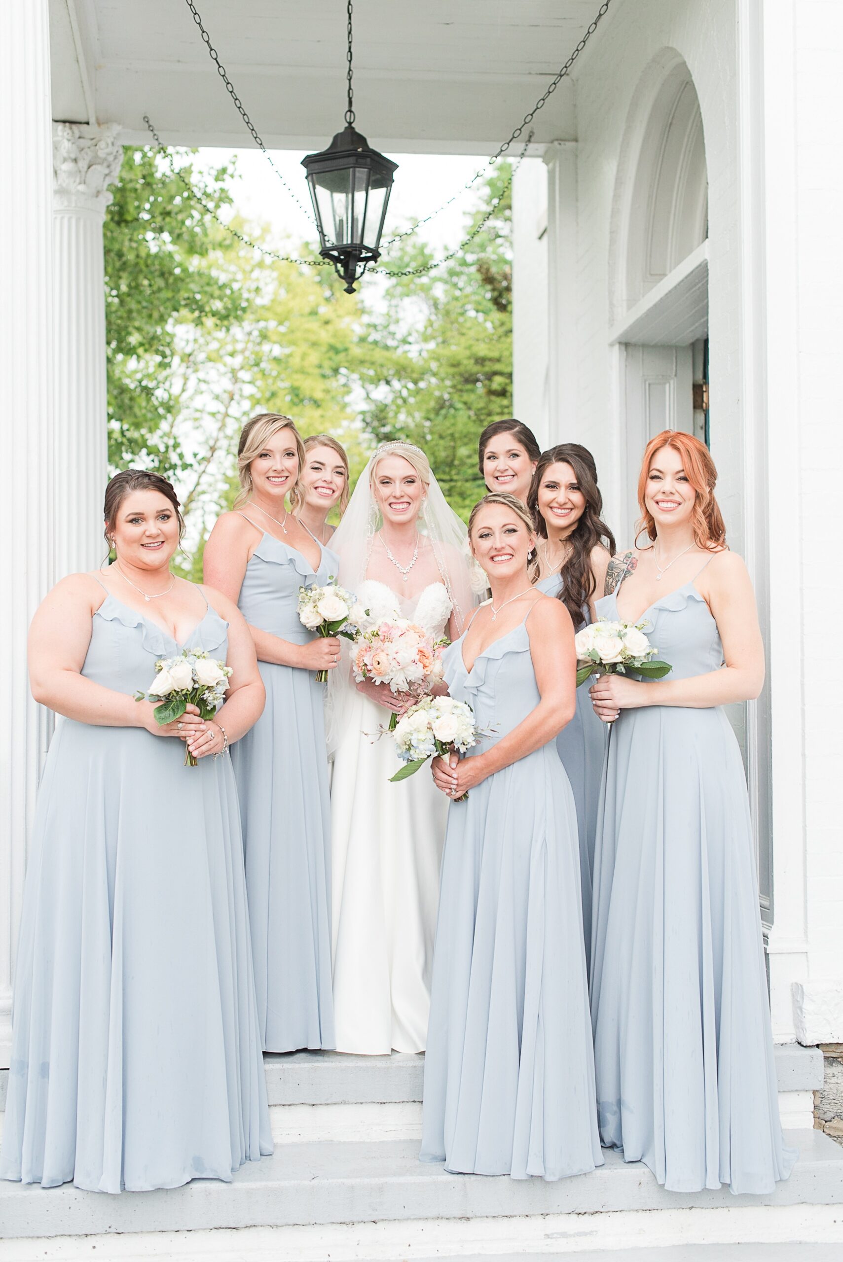 A bride stands with her bridesmaids on a white porch holding their bouquets at the Ceresville Mansion Wedding venue