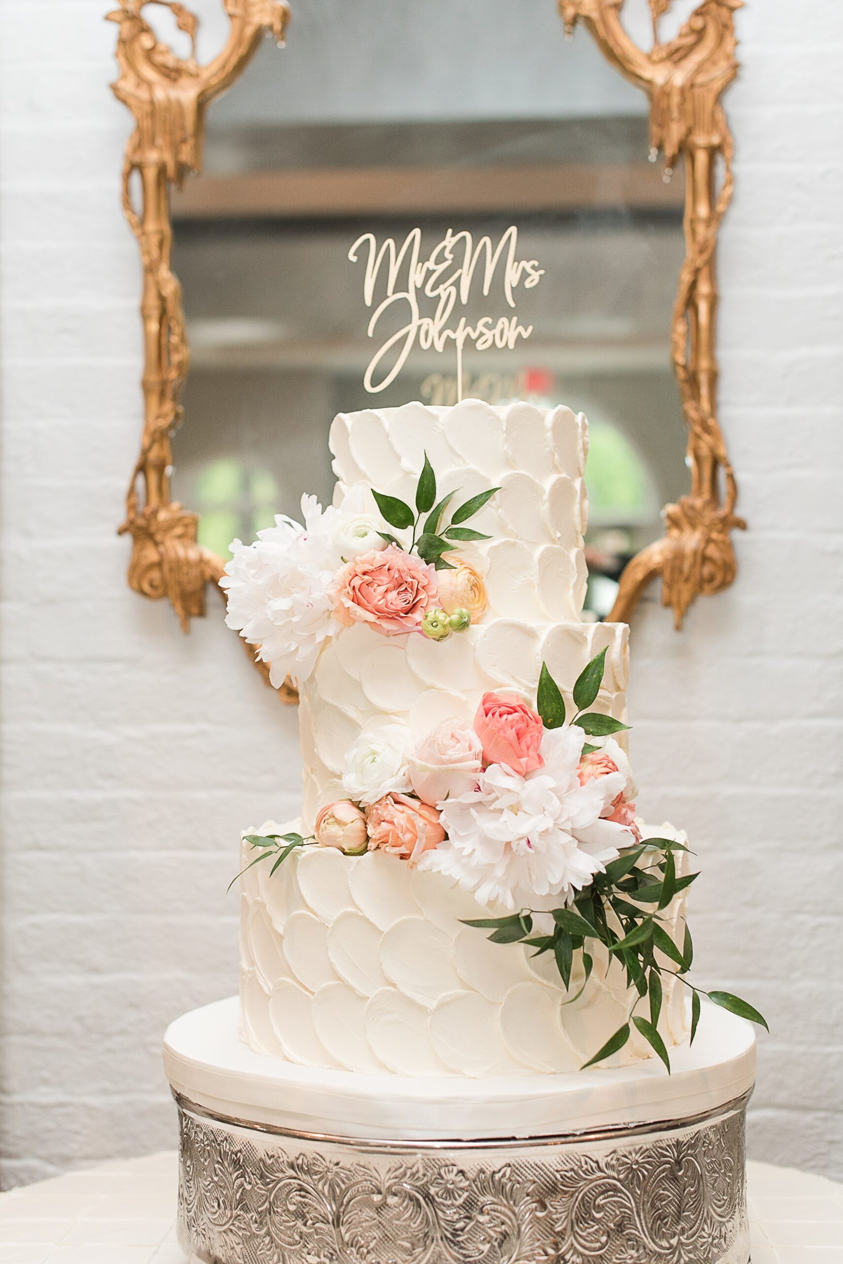 Details of an ornate three tier cake with florals on a silver stand