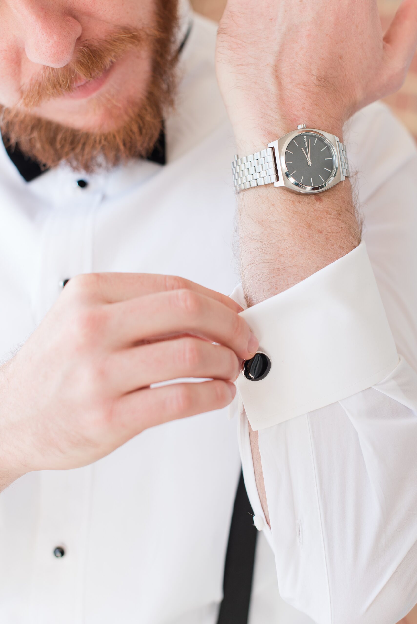 A groom adjusts his cufflink while getting ready for his Cloisters Castle Wedding