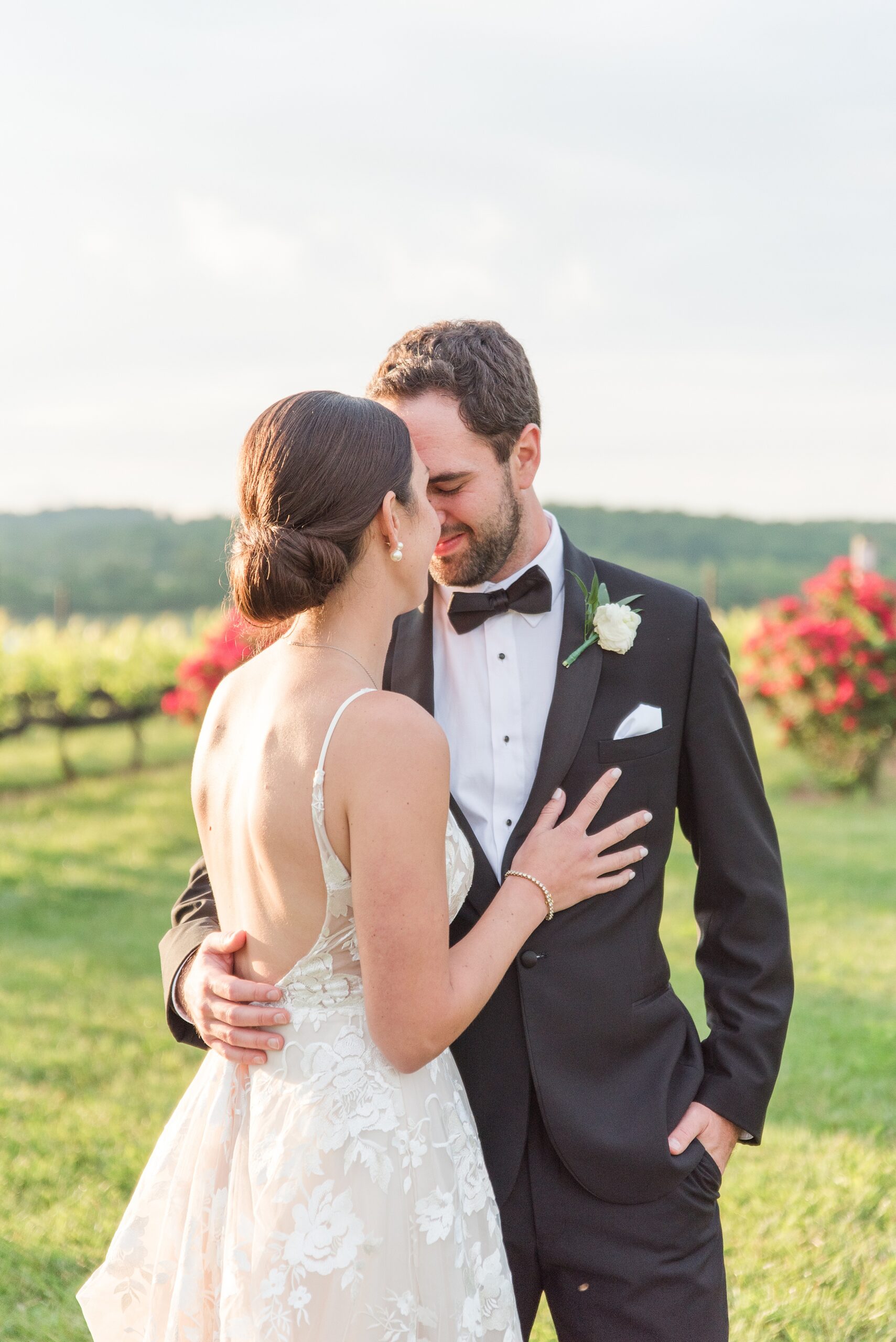 Newlyweds share an intimate moment on a lawn with blooming bushes at sunset