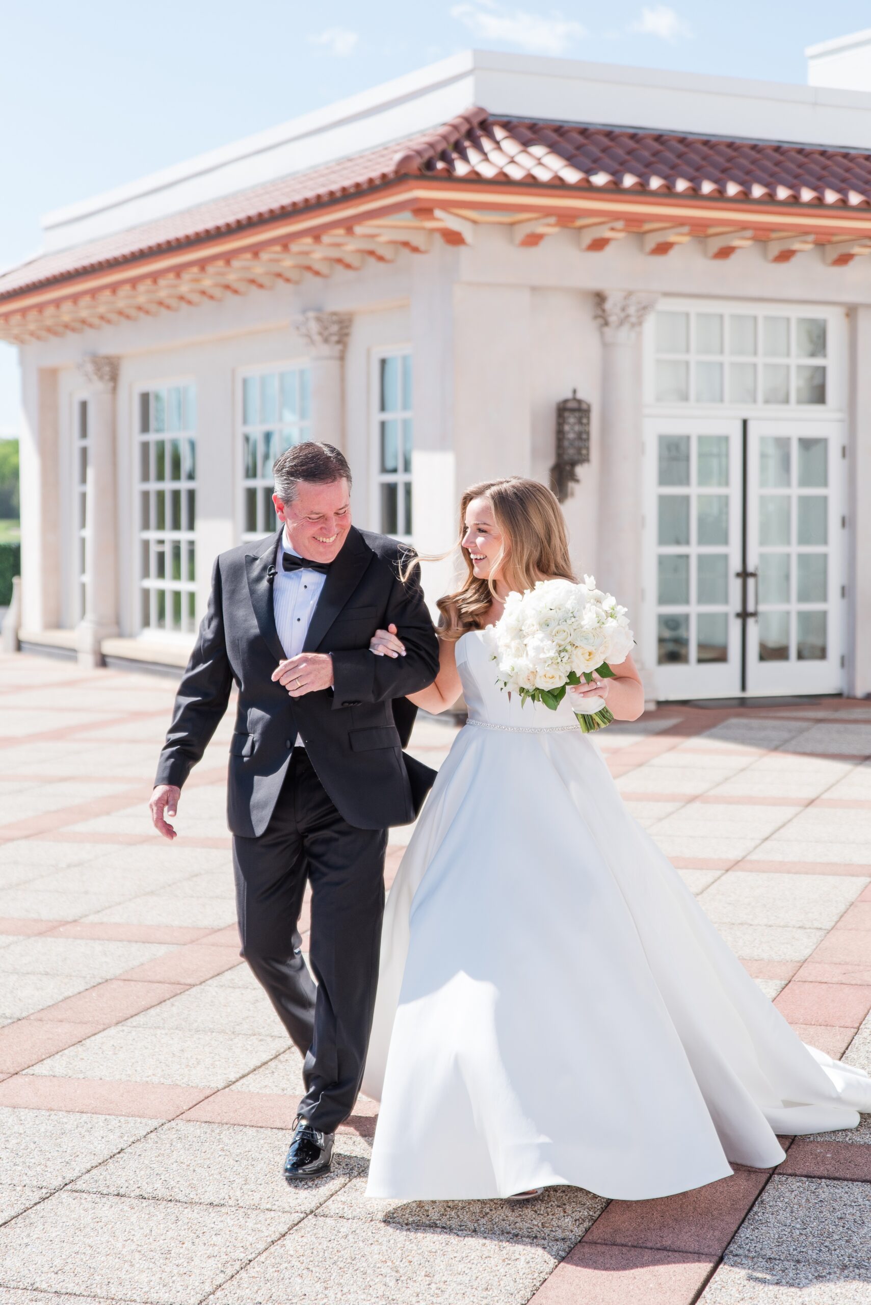A father in a black suit walks his daughter down the aisle to her wedding