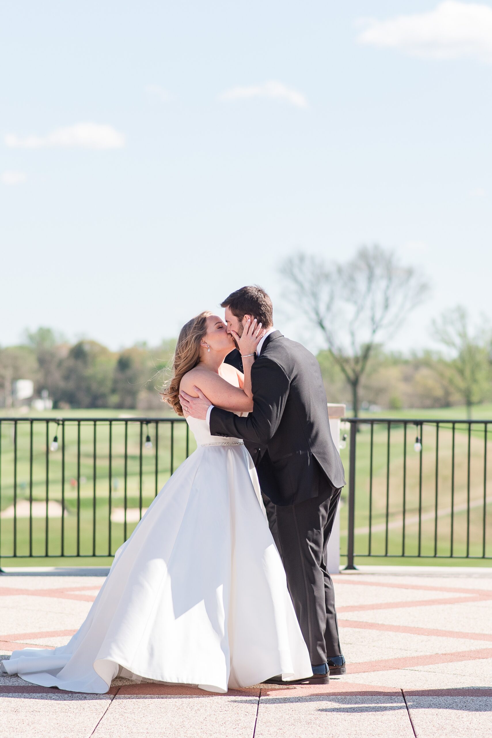 Newlyweds kiss while standing on a balcony overlooking the Congressional Country Club Wedding venue golf course