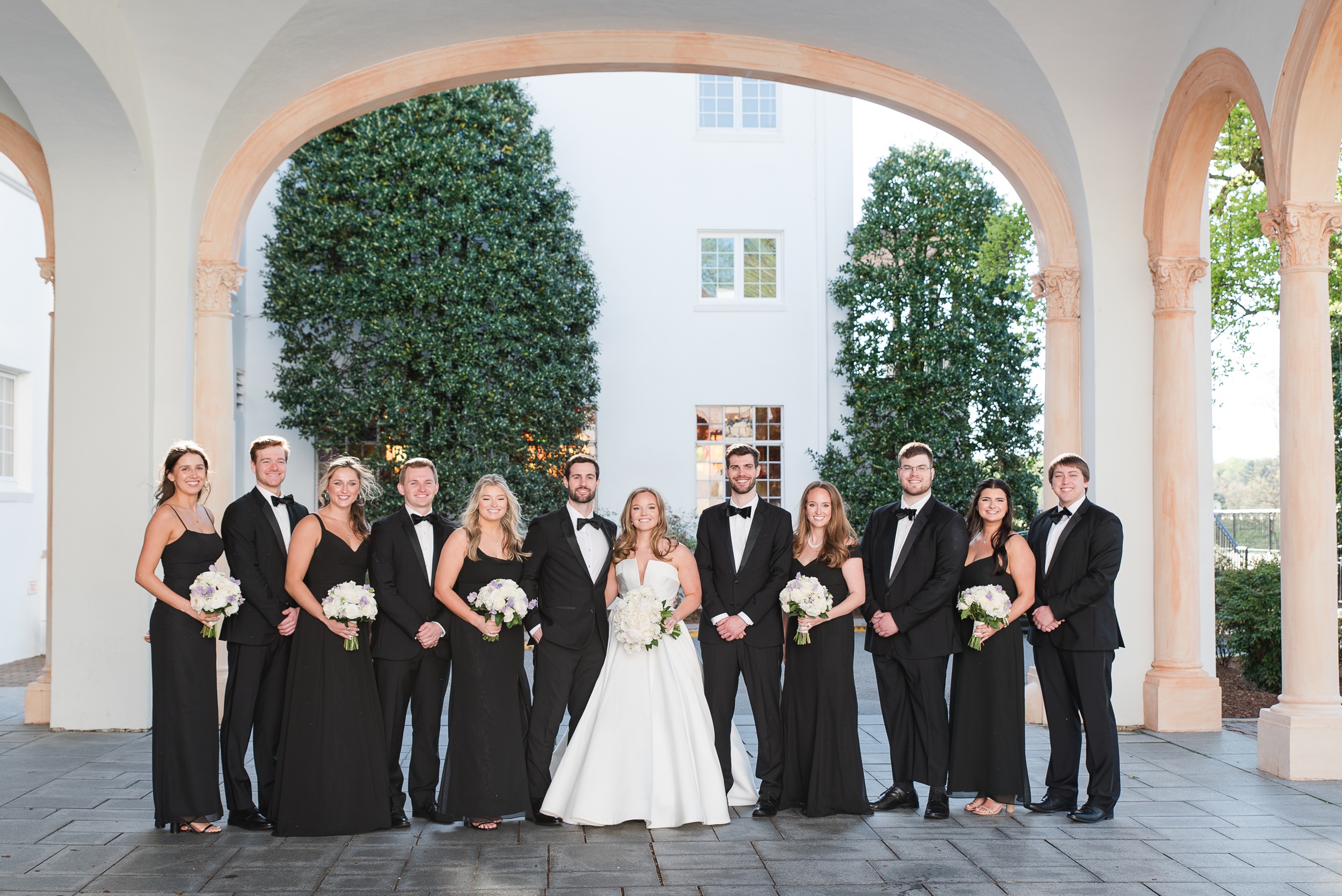 Newlyweds stand in a covered driveway with their wedding party