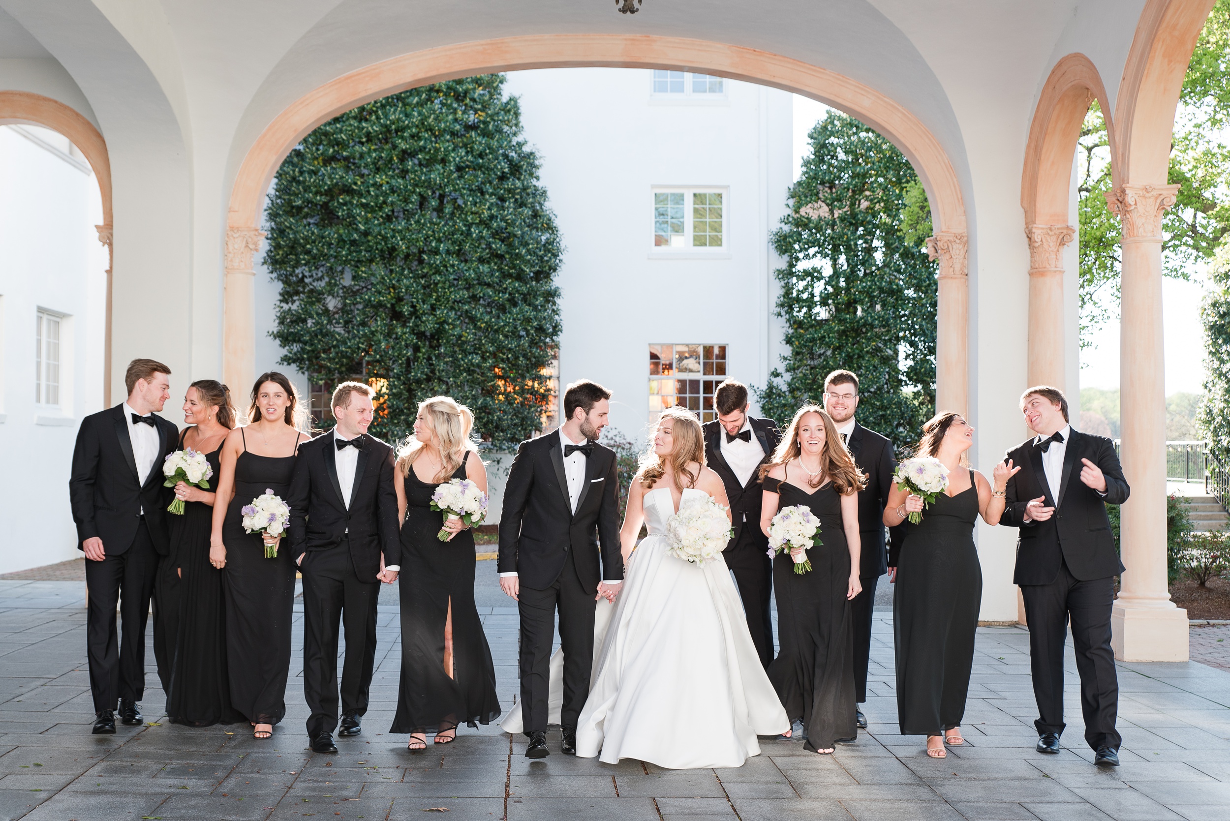 Newlyweds hold hands while walking with their large bridal party