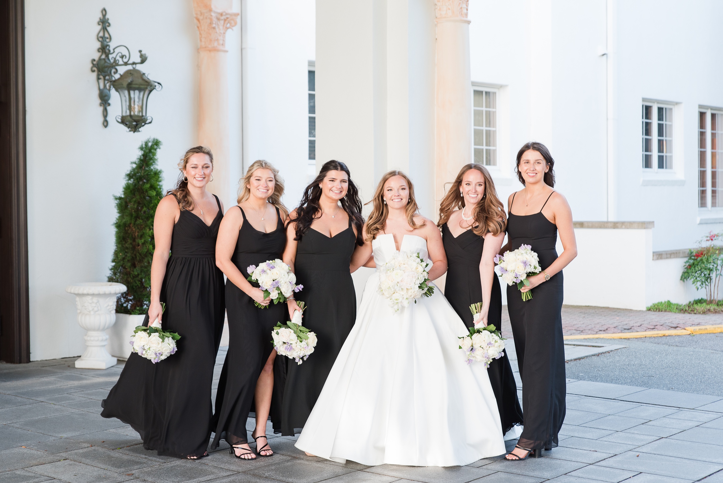 A bride stands with her bridesmaids in black dresses under the driveway cover.